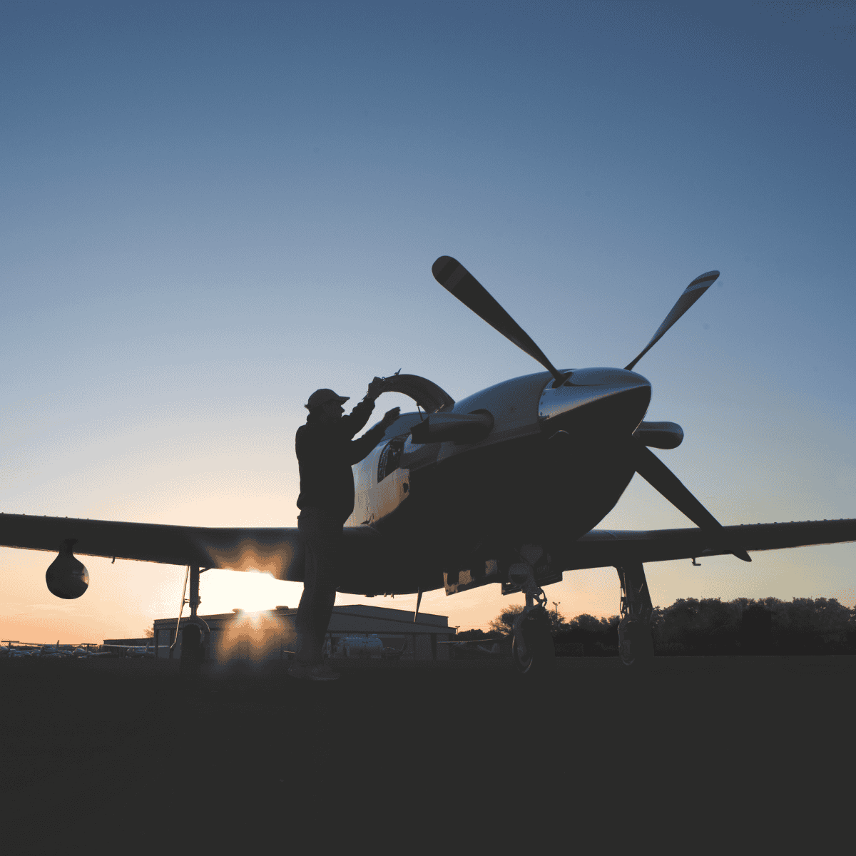 Person inspecting small airplane at sunset