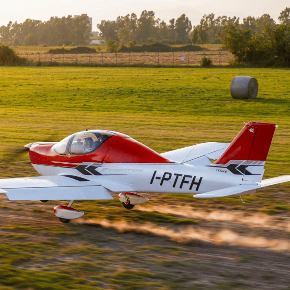 Small red airplane landing on grass runway