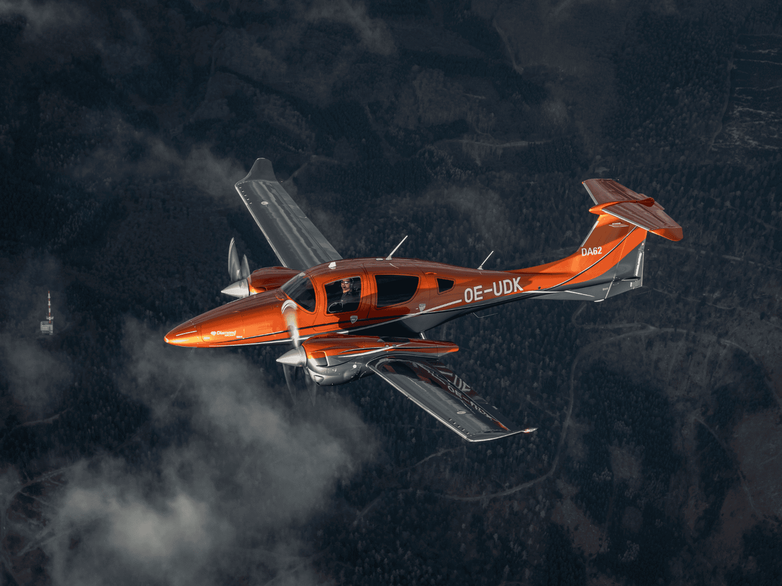 Orange twin engine airplane flying above forest