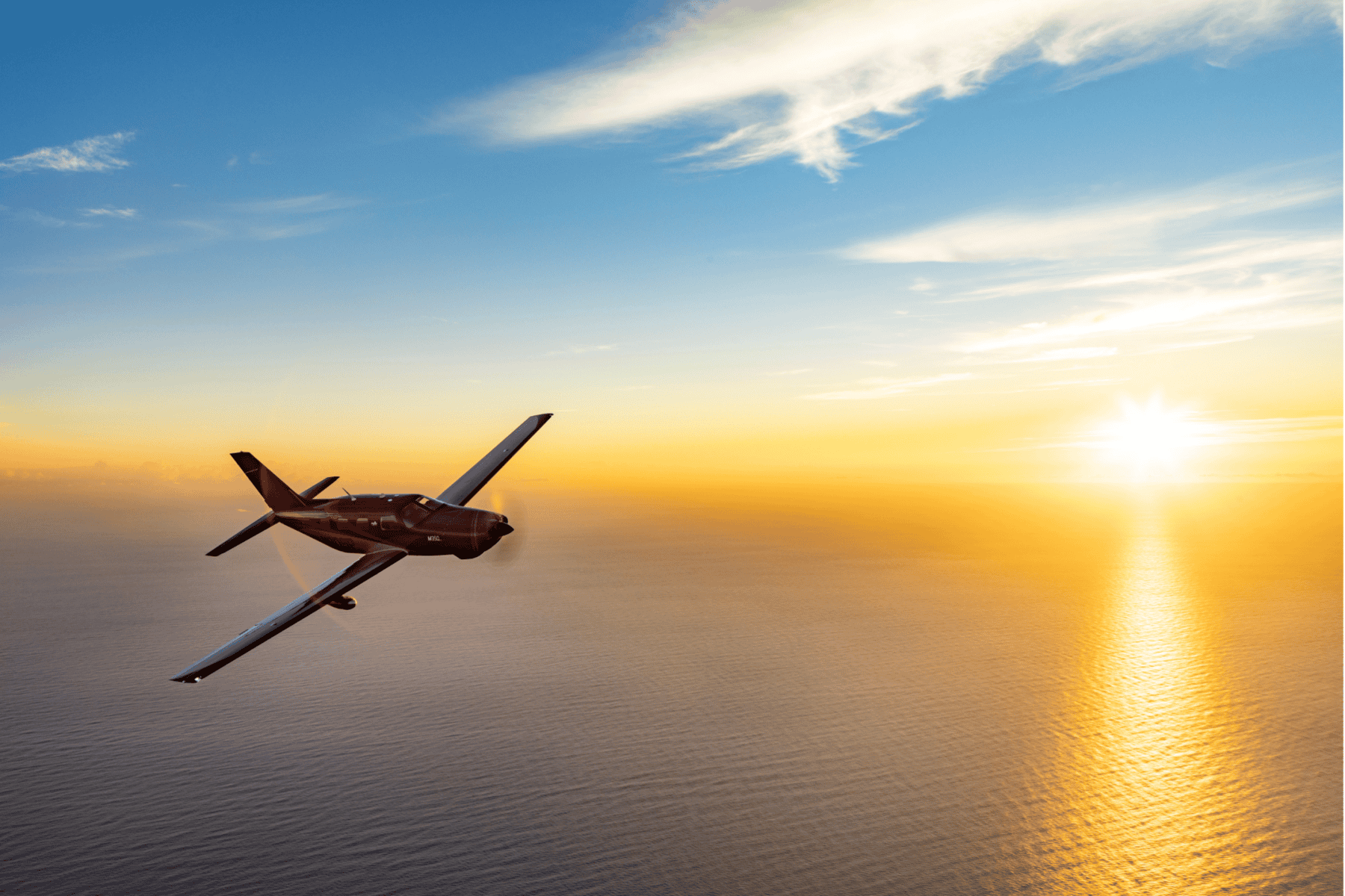 Airplane flying over ocean at sunset.