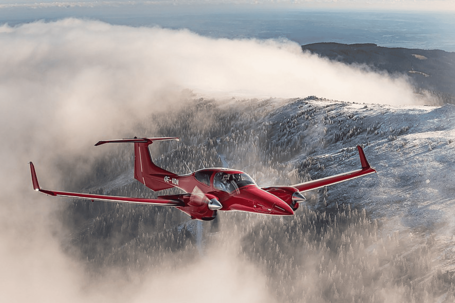 Red airplane flying over snowy mountains and clouds.