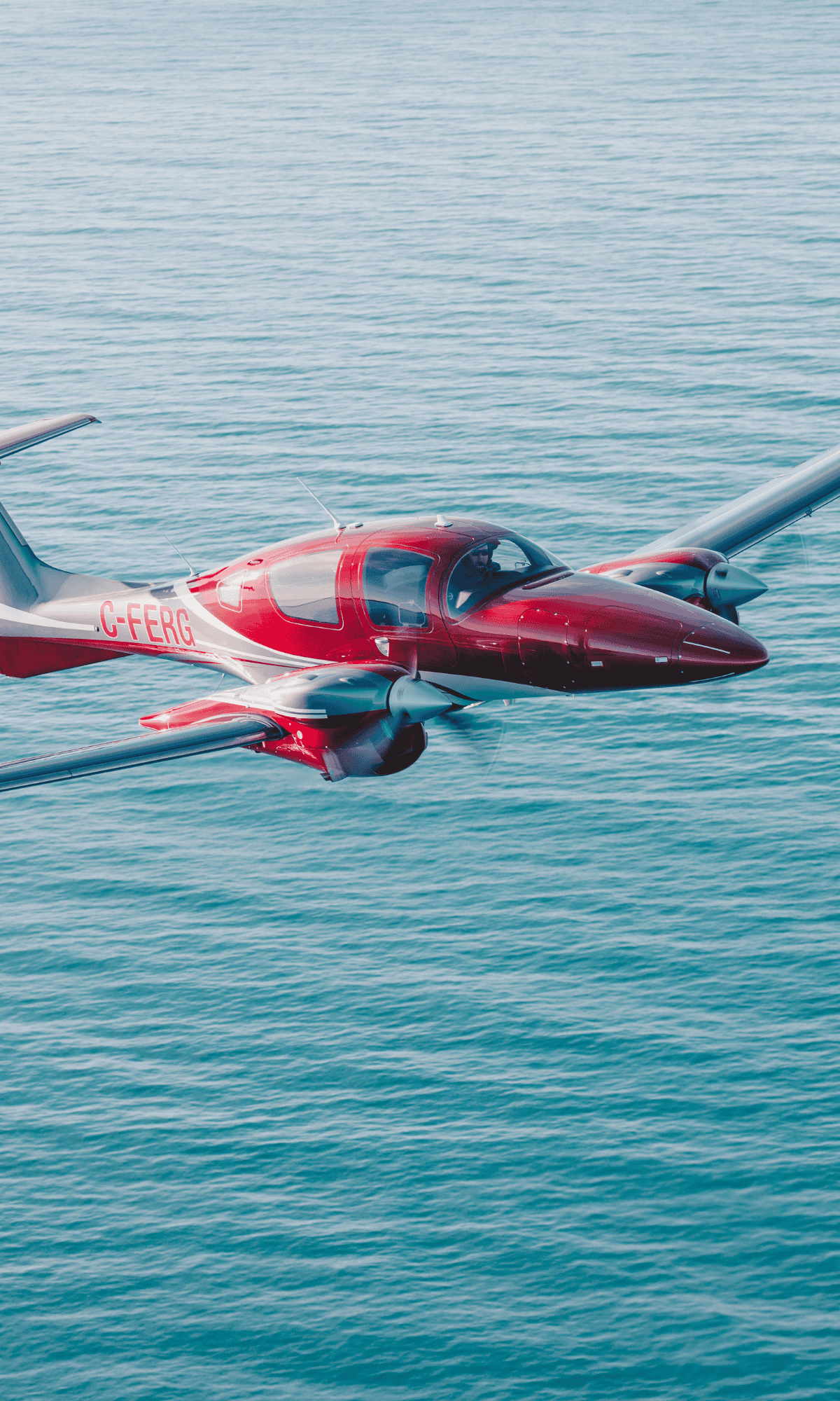 Red and silver airplane flying over the ocean