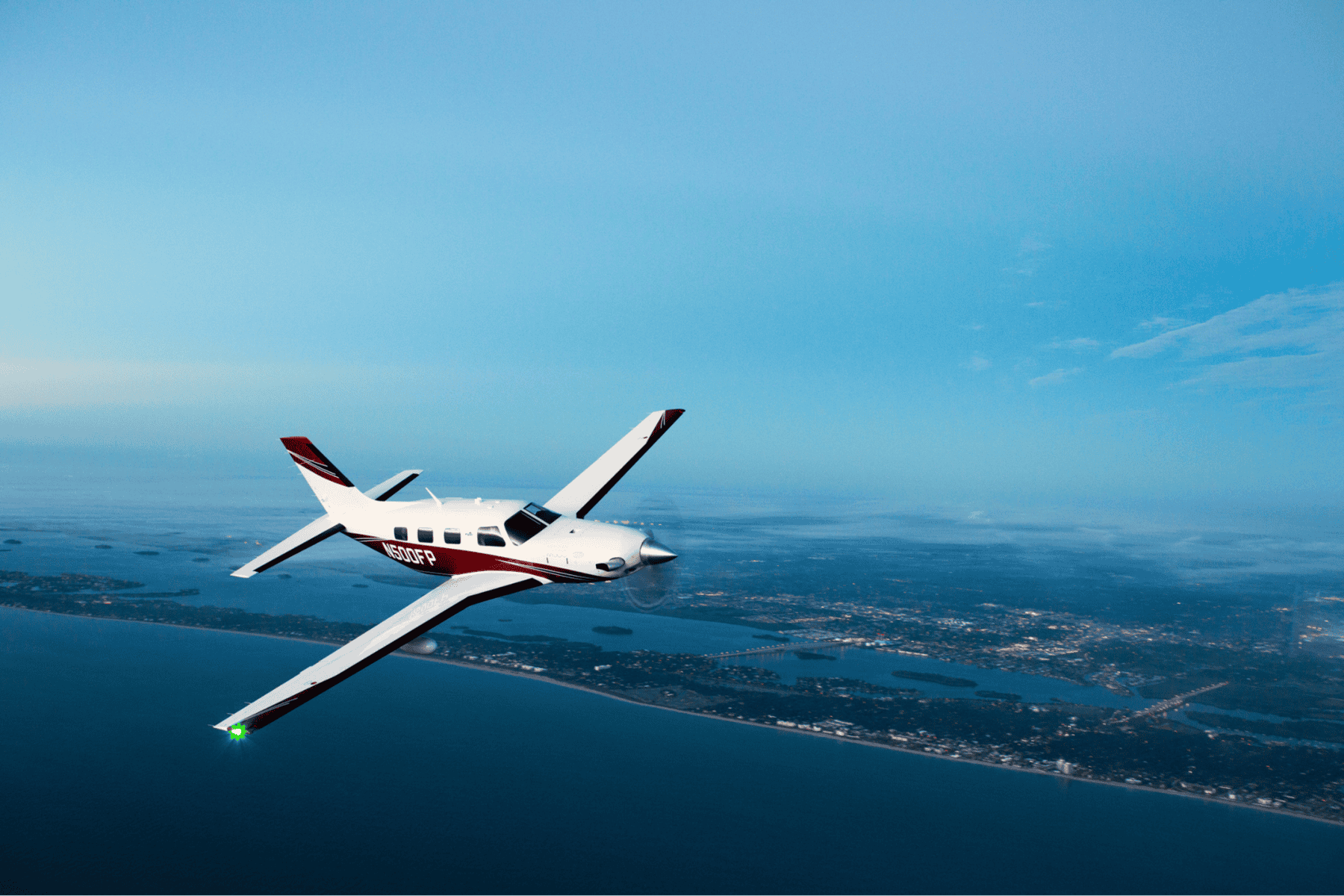Small aircraft flying over coastline at dusk.