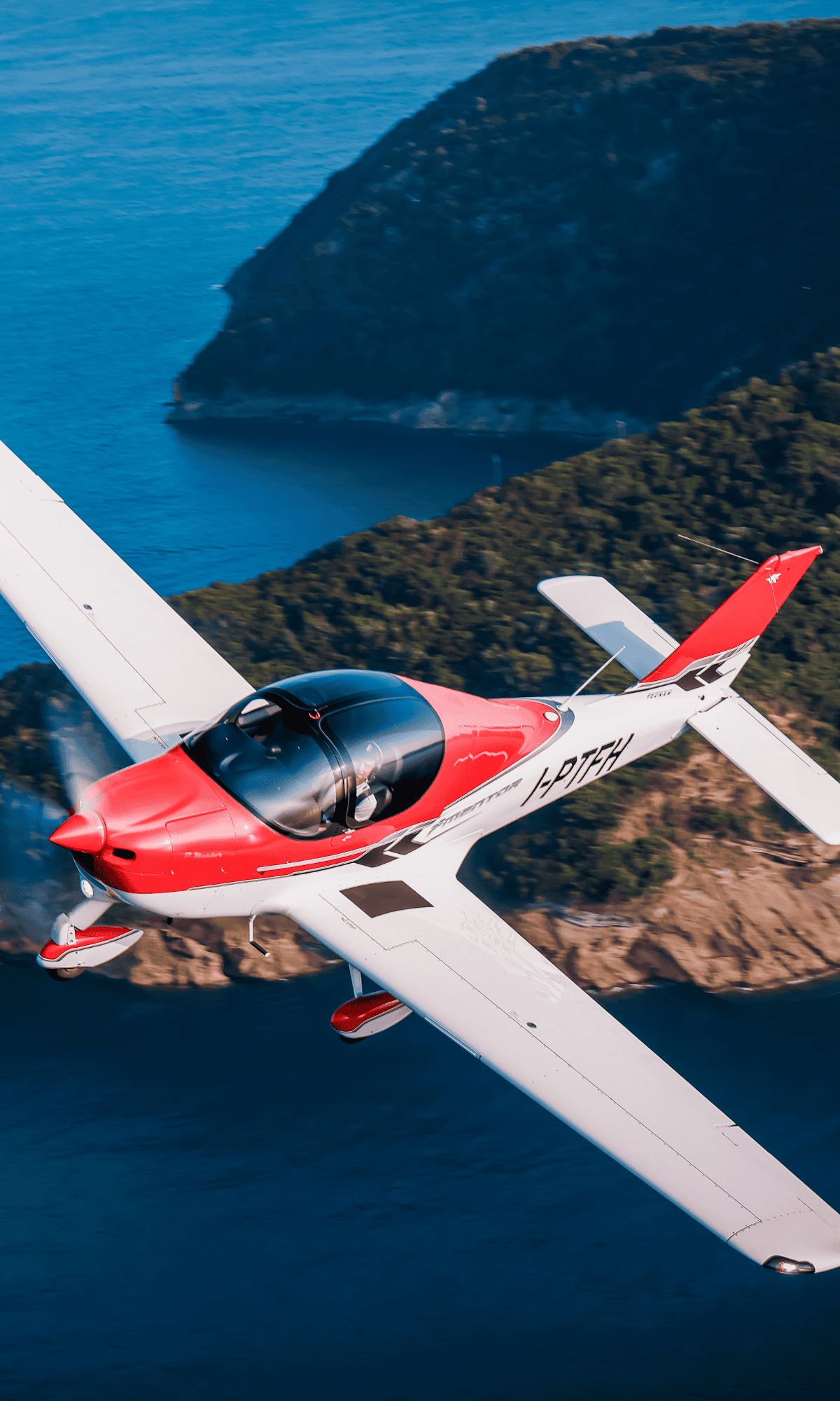 Red and white airplane flying over a coastline