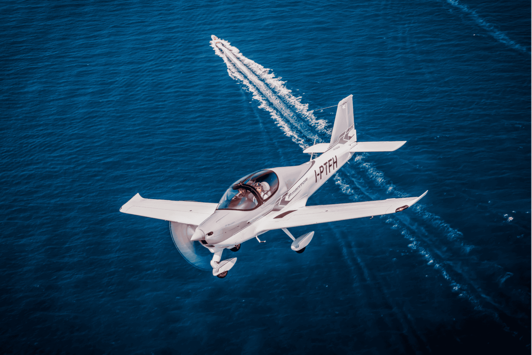 Small airplane flying over ocean with boat below.