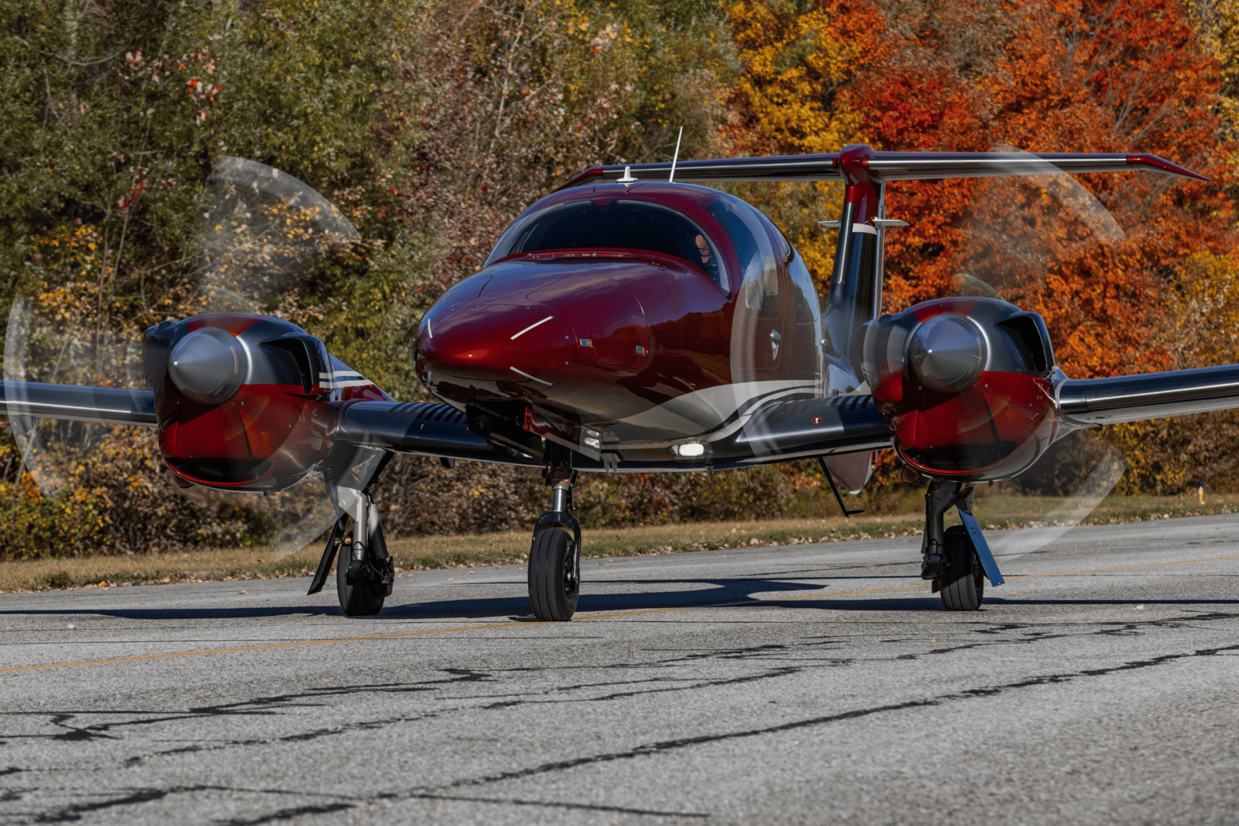 Red airplane on runway with autumn trees background.