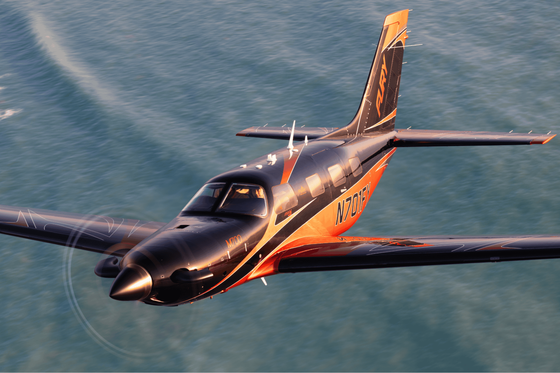 Black and orange airplane flying over the ocean.