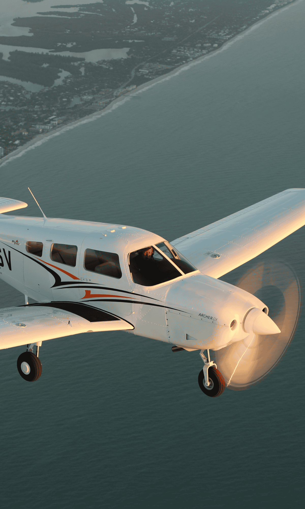 Small airplane flying over coastline at sunset