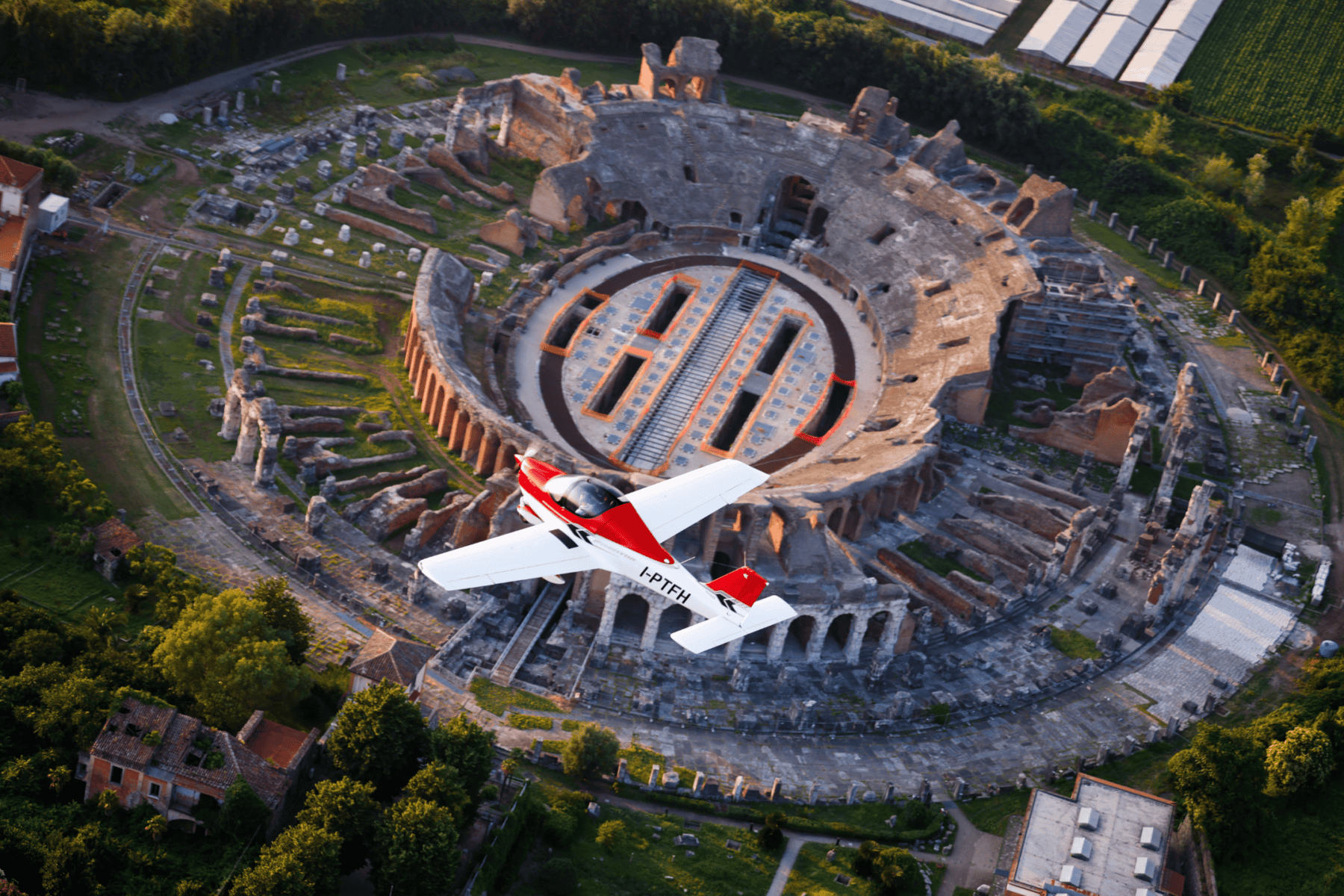 Small airplane flying over ancient amphitheater.