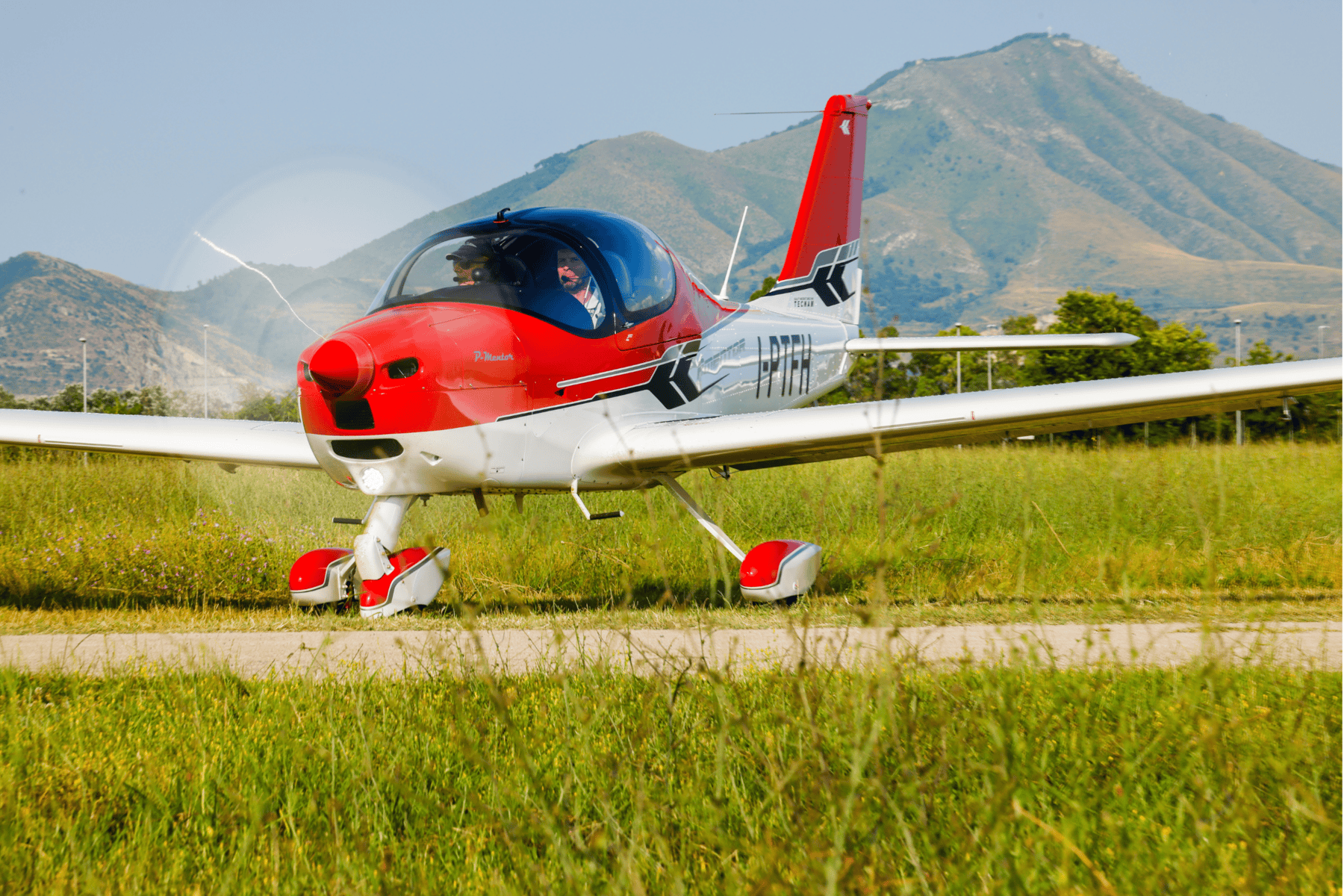 Red and white plane on grassy field with mountains