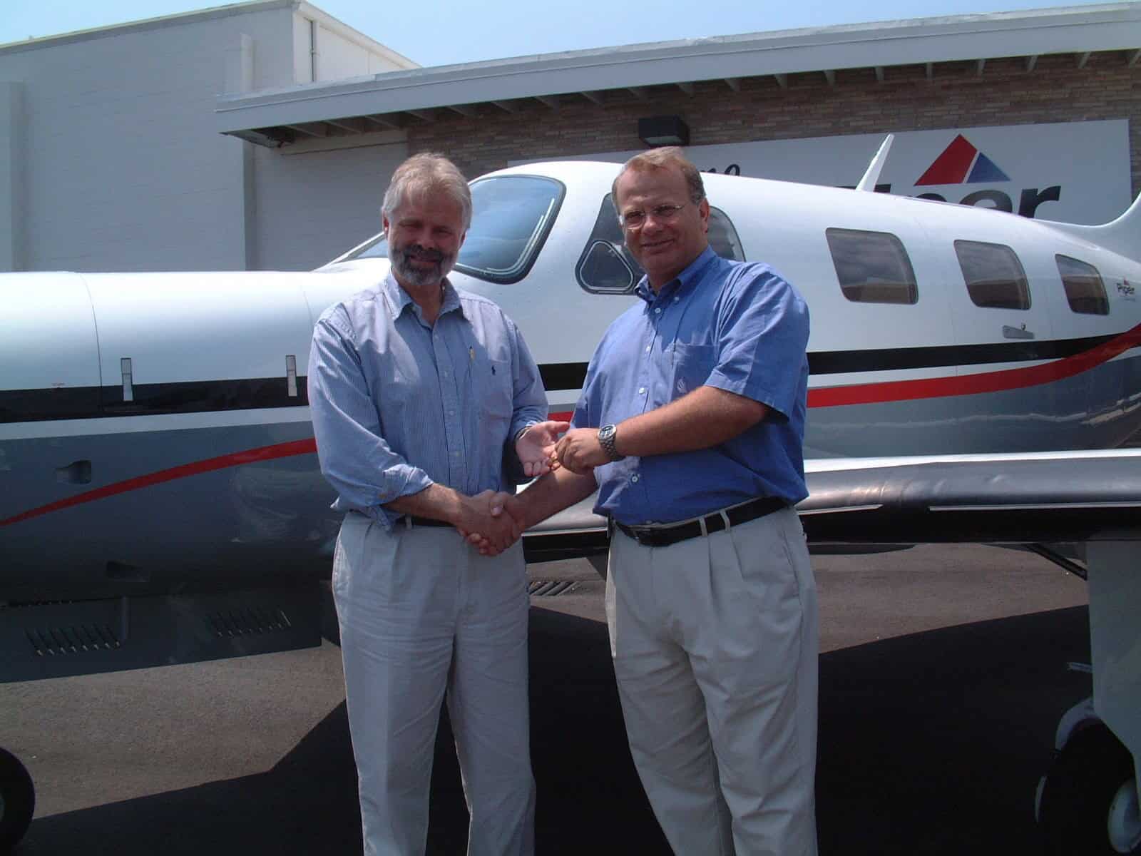 Two men shaking hands beside an airplane