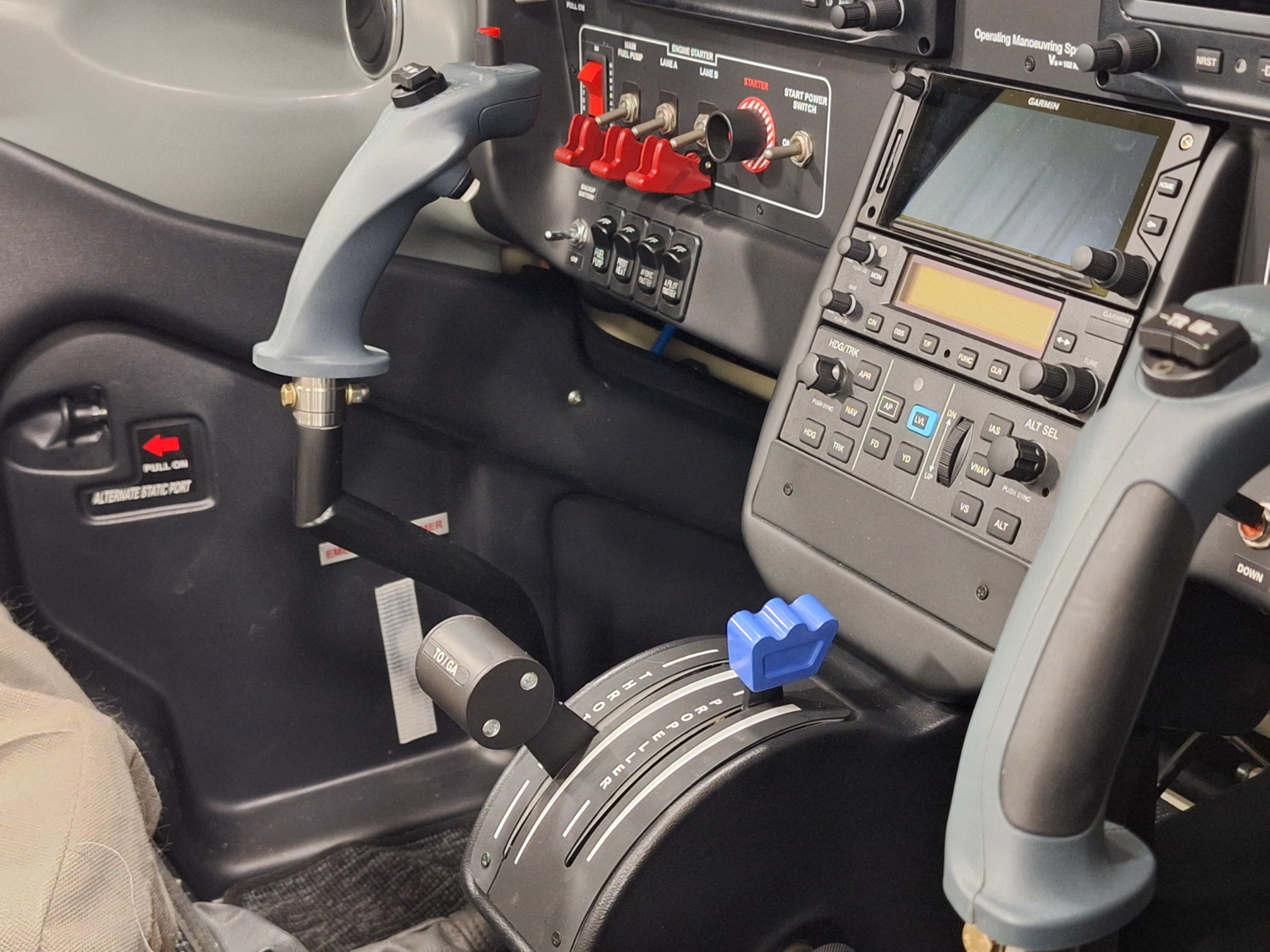 Aircraft cockpit interior with gray control stick, red toggle switches, and Garmin avionics display.