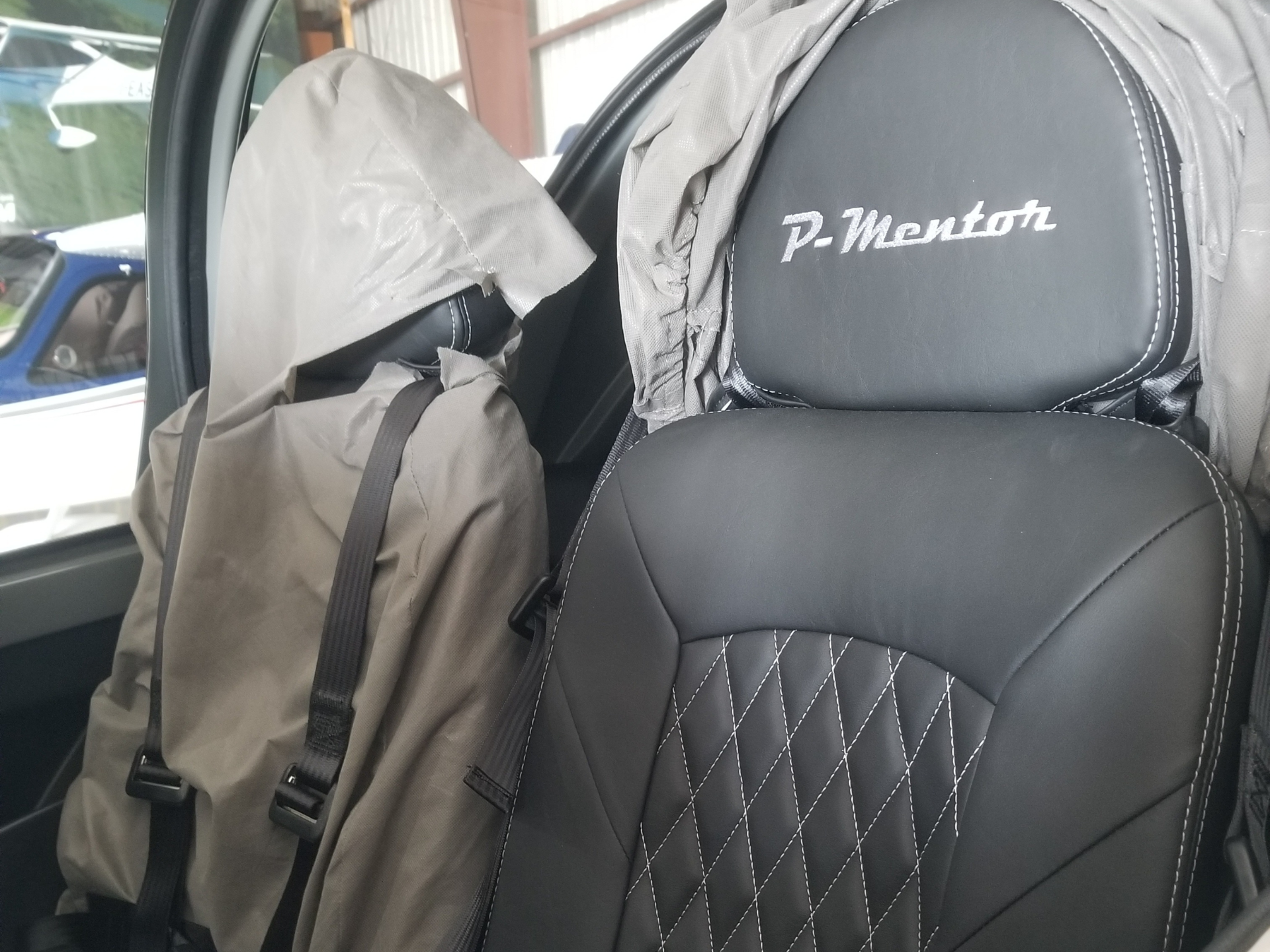 Car interior: black leather seat with white stitching and embroidered 'P-Mentor' on the headrest image detail