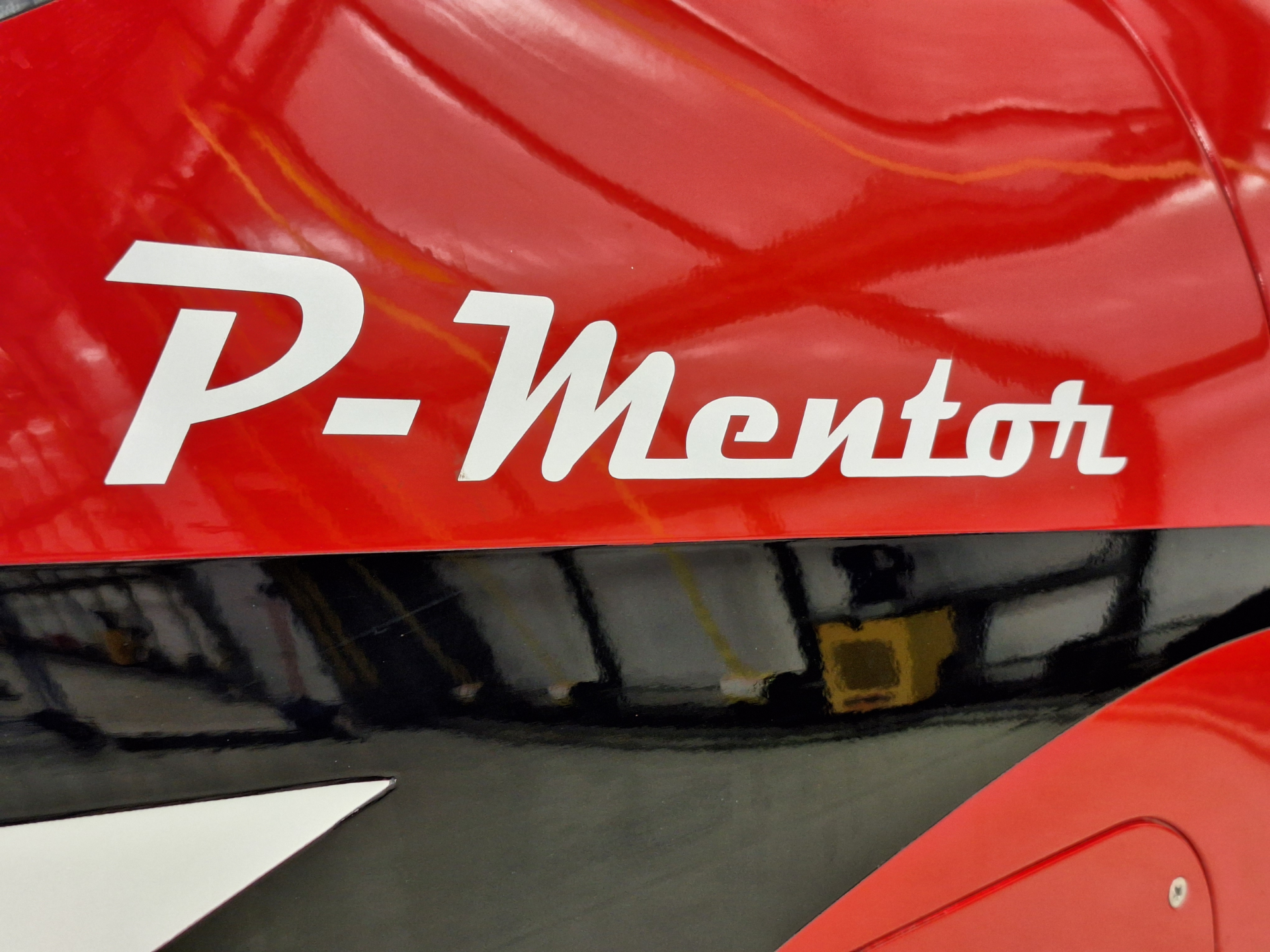 Close-up of a red glossy vehicle surface with a white cursive logo partially visible (reads 'P-Mento').