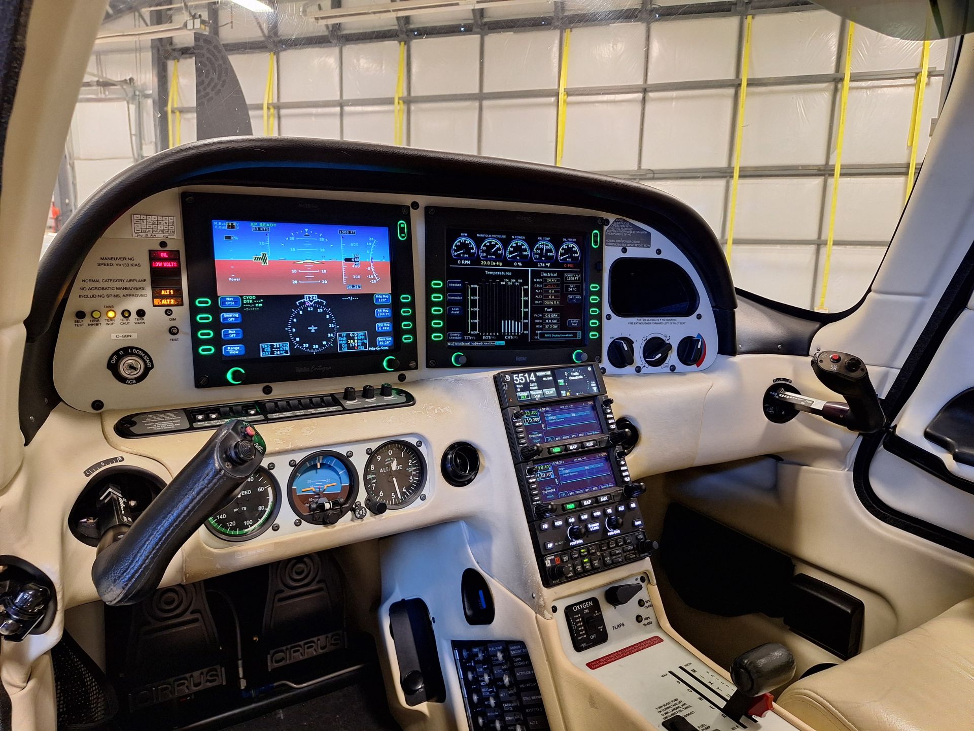 Cockpit of a small aircraft with multiple digital flight displays, a yoke, and center console inside a hangar.