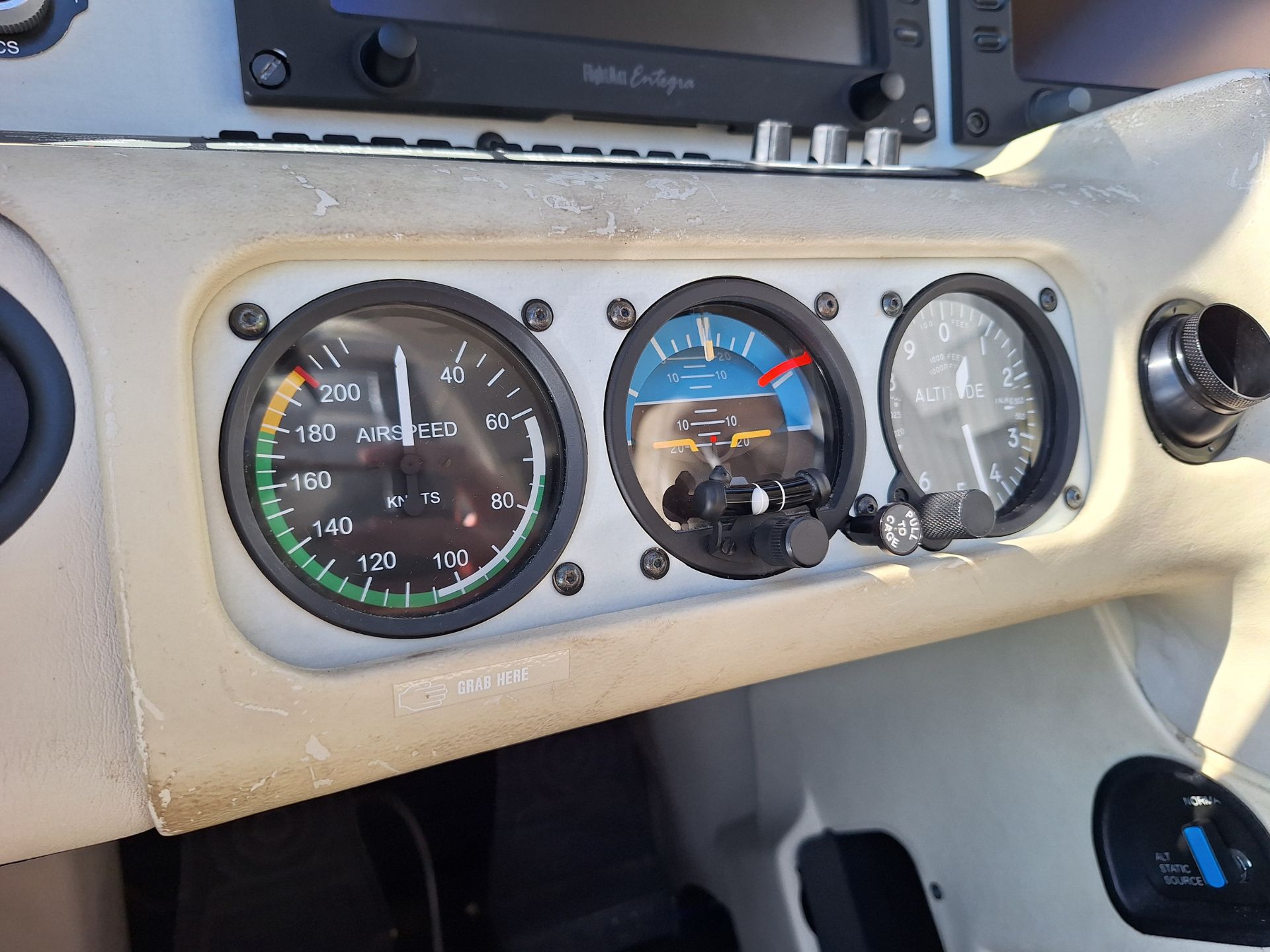 Cockpit instrument cluster showing airspeed gauge, attitude indicator, and altimeter on a worn beige panel.