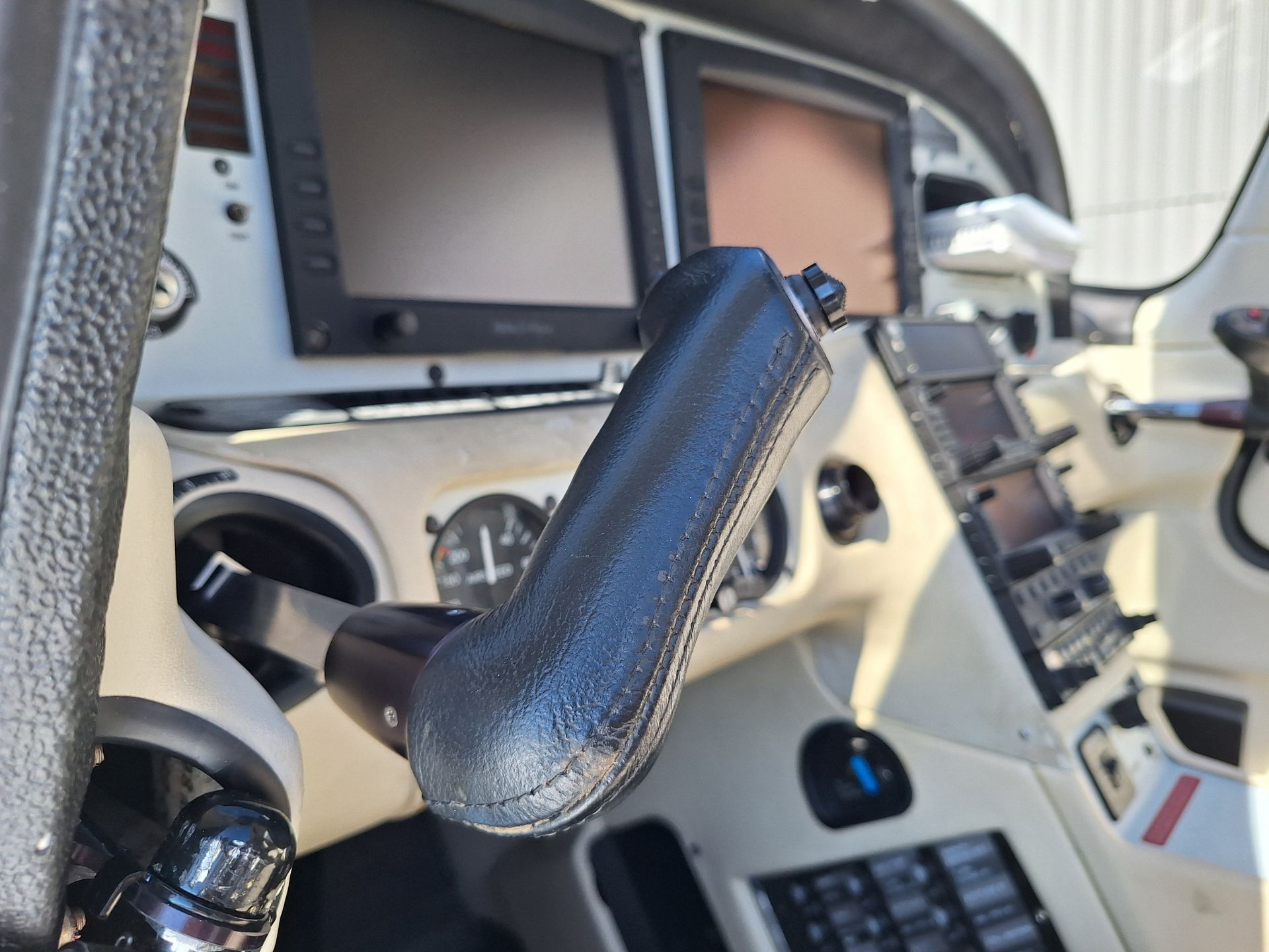 Close-up of an airplane cockpit yoke with large avionics displays and control panels in view.