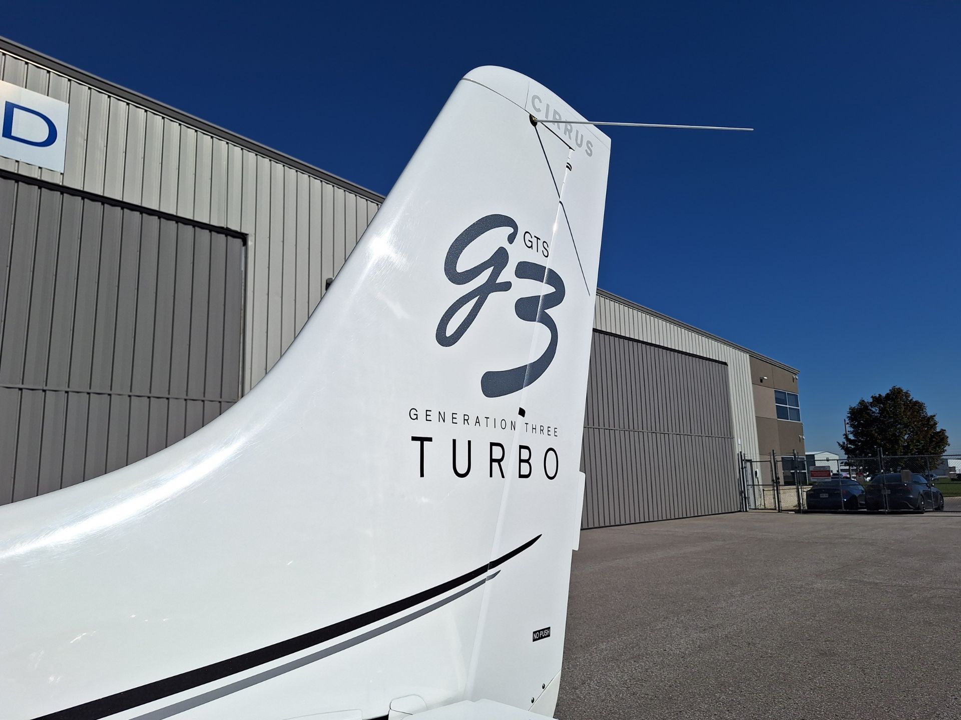White airplane tail with 'GTS' branding and 'TURBO' text, beside a gray hangar under a clear blue sky.