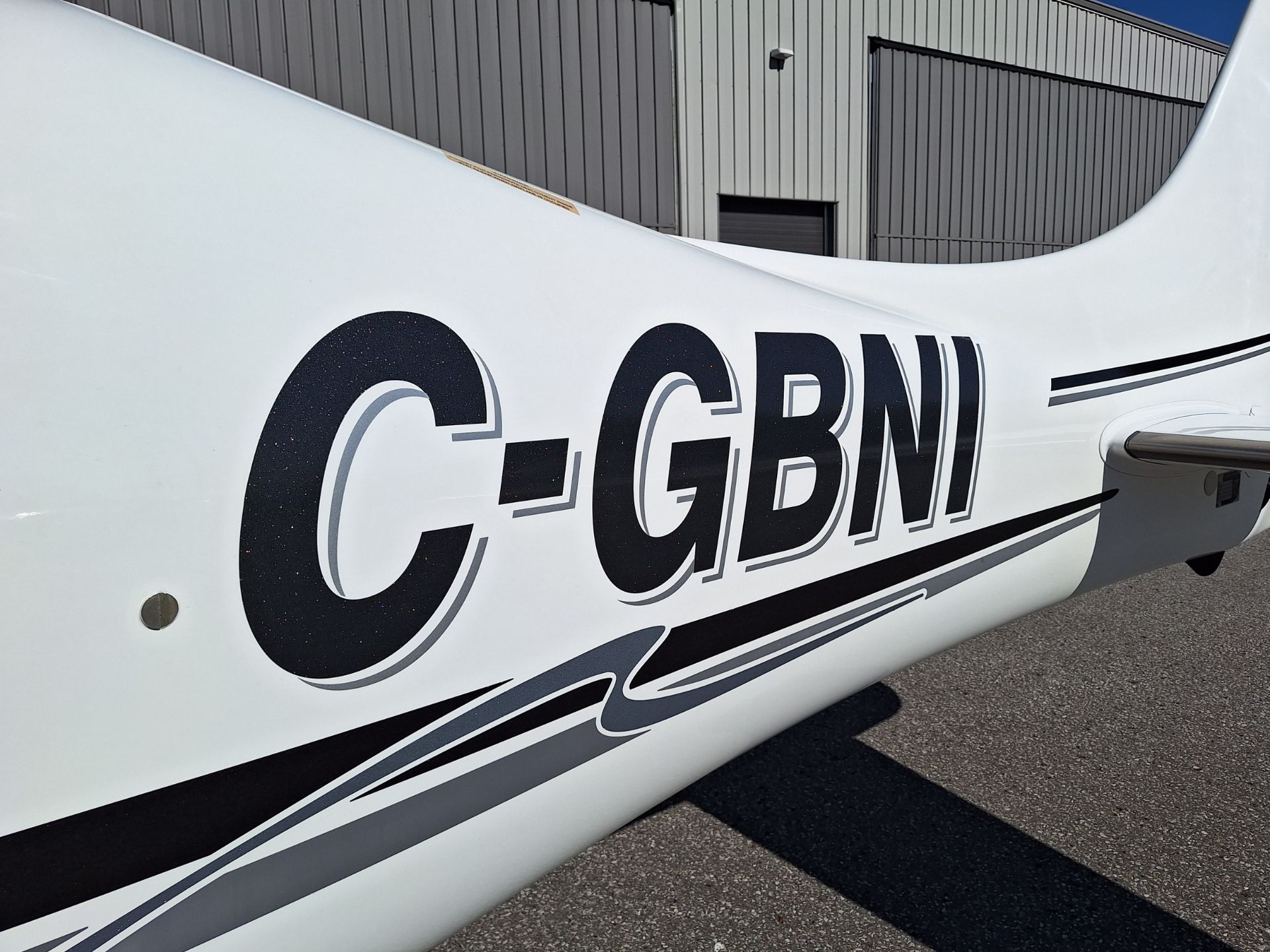 Aircraft fuselage with large black registration letters 'C-GBNI' and gray decorative stripes; hangar in the background.