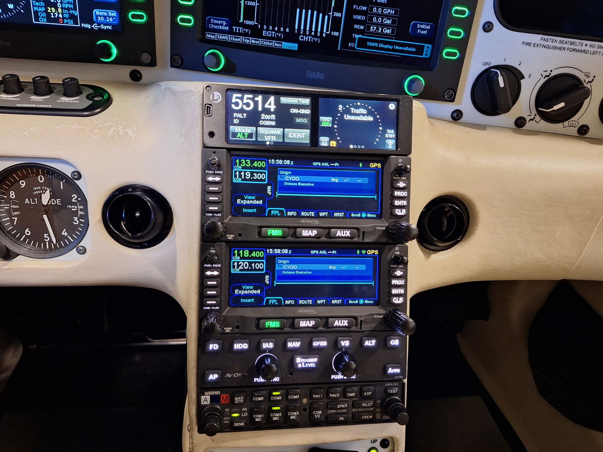Pilot cockpit panel with stacked avionics displays and green-backlit controls, including navigation screens and a large analog gauge on the left side of the panel.