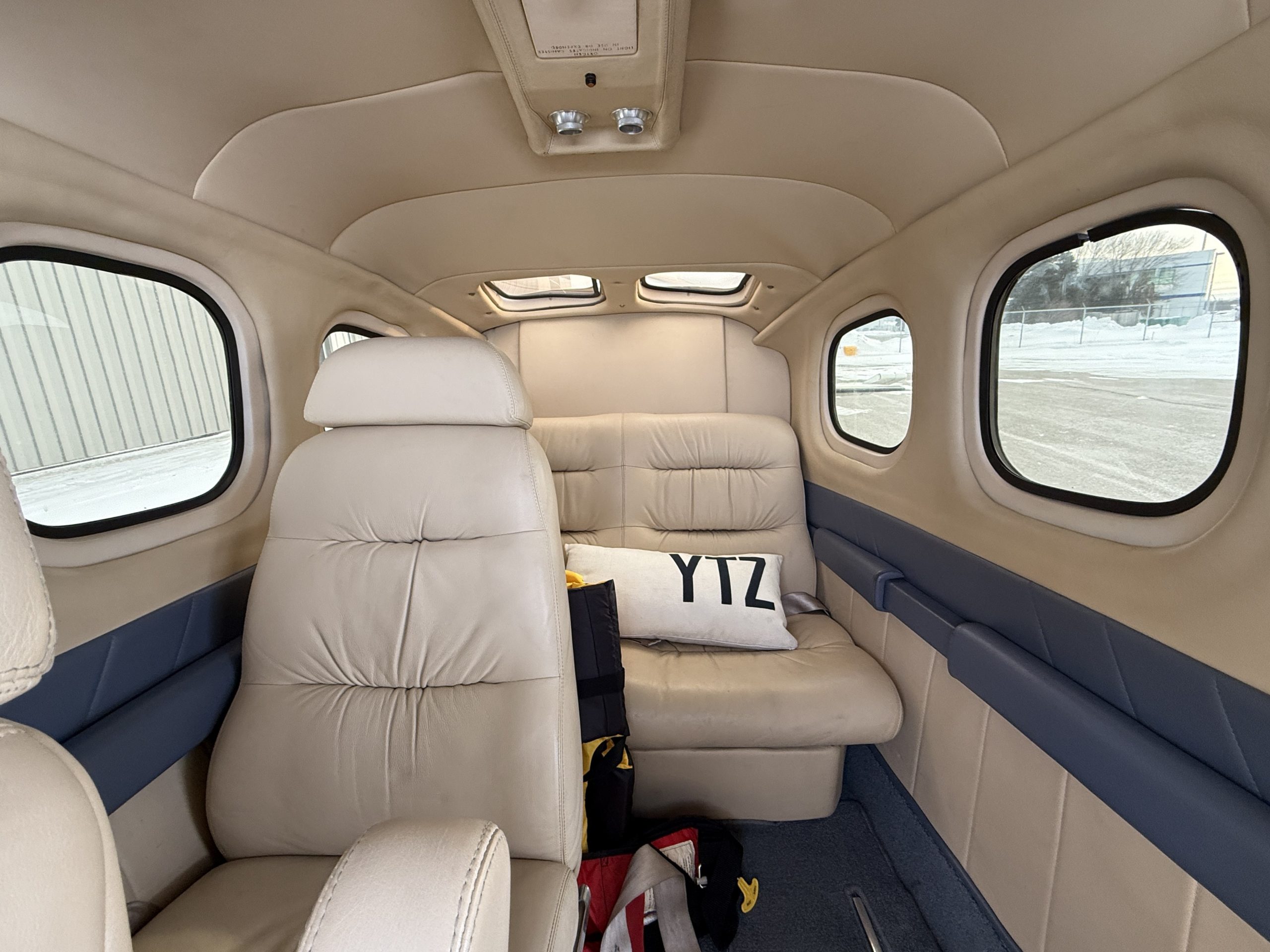 Interior of a small aircraft cabin with beige leather seats and large windows bags and gear on the floor between seats