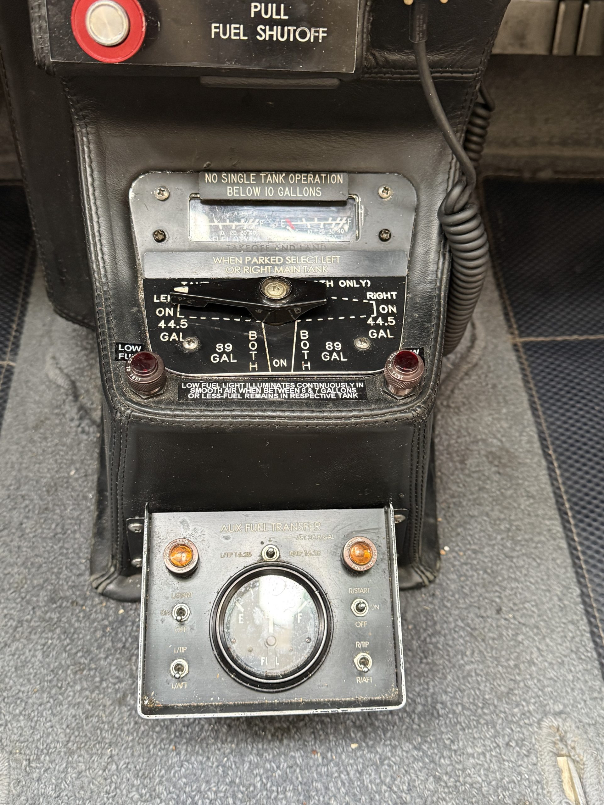 Vintage aircraft center console showing a fuel gauge and transfer controls with a No single tank operation below 10 gallons warning panel behind it
