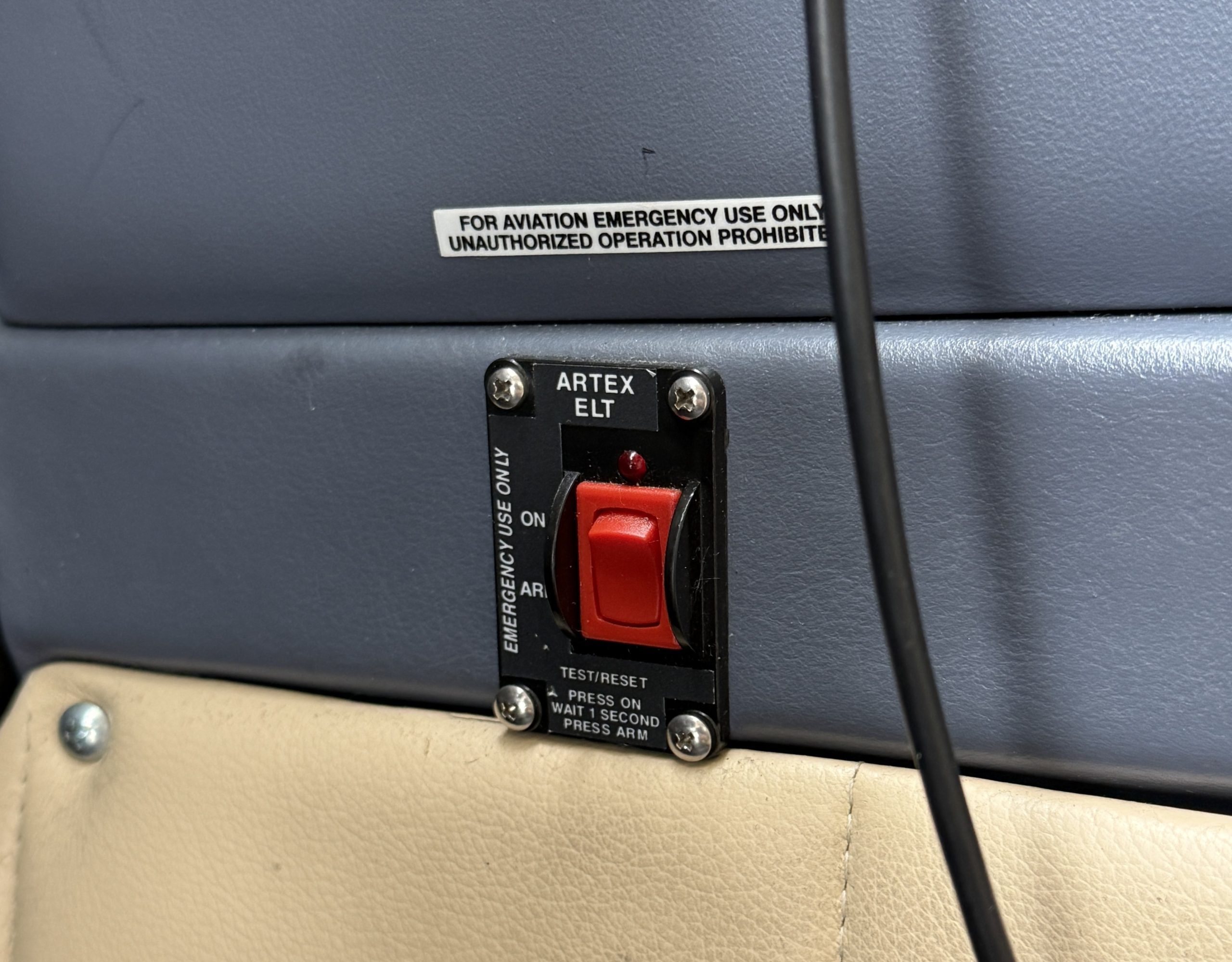 Close up of a blue panel with an emergency switch label that reads FOR AVIATION EMERGENCY USE ONLY UNAUTHORIZED OPERATION PROHIBITED and an ARTEX ELT switch nearby