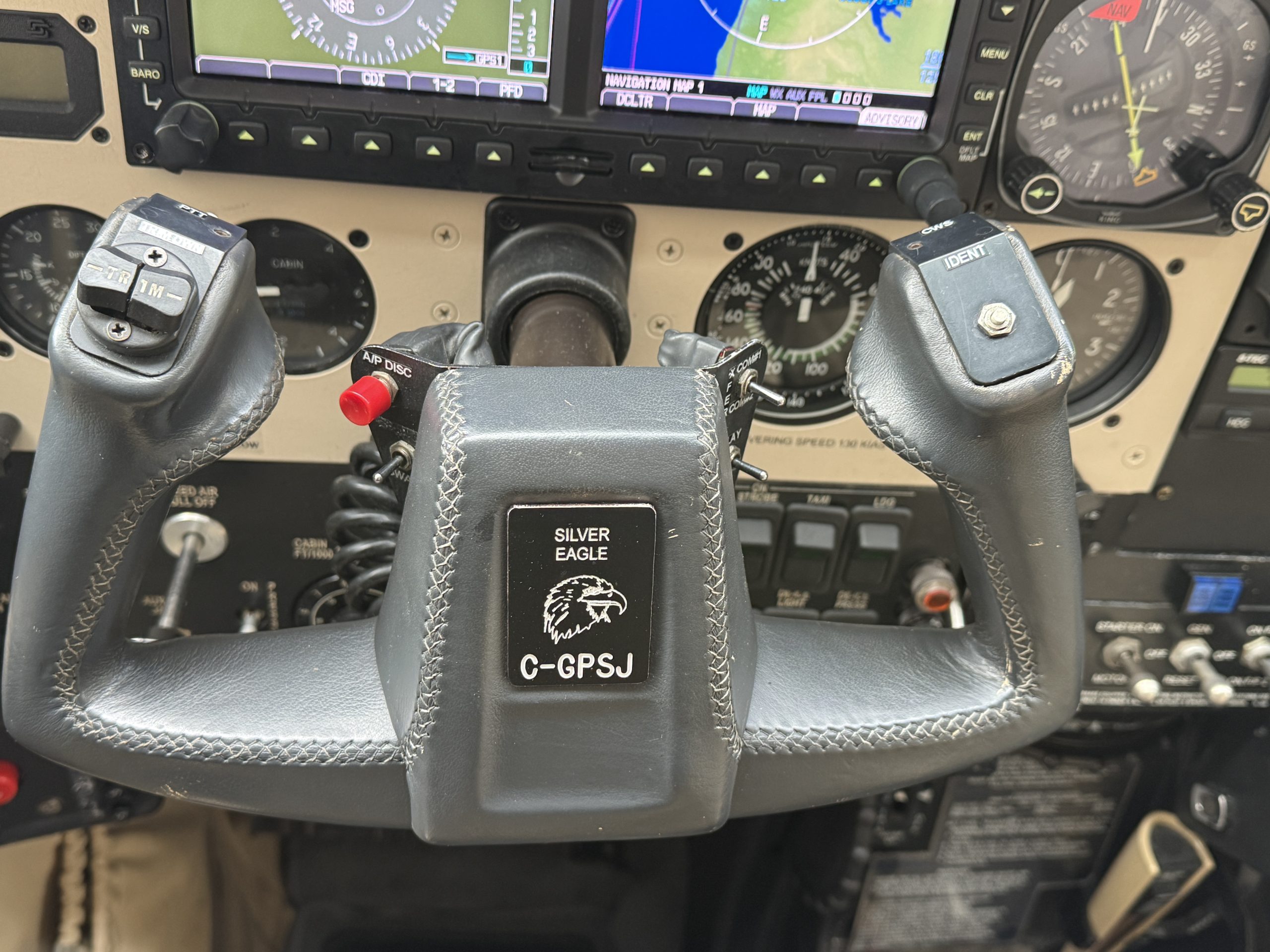 Dual yokes in a small aircraft cockpit with Garmin navigation screens above and a central instrument panel including a prominent GPS unit labeled C GPSJ and a leather wrapped control column