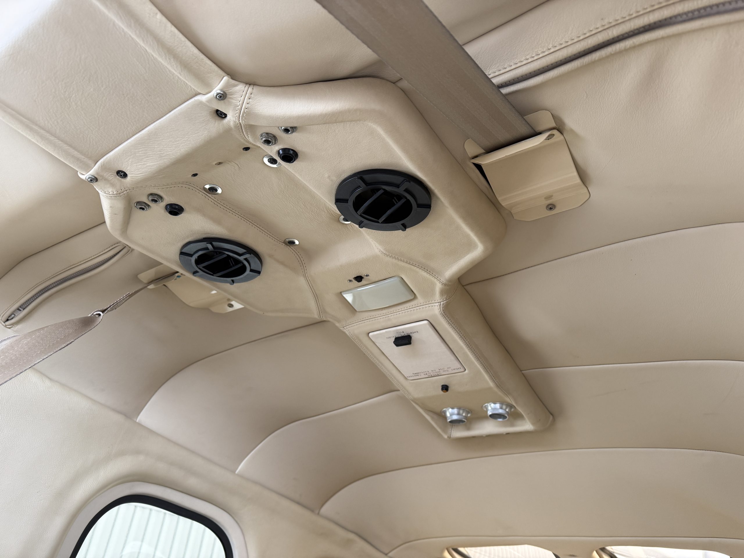 Close up of a beige airplane cabin ceiling panel with round air vents and fasteners