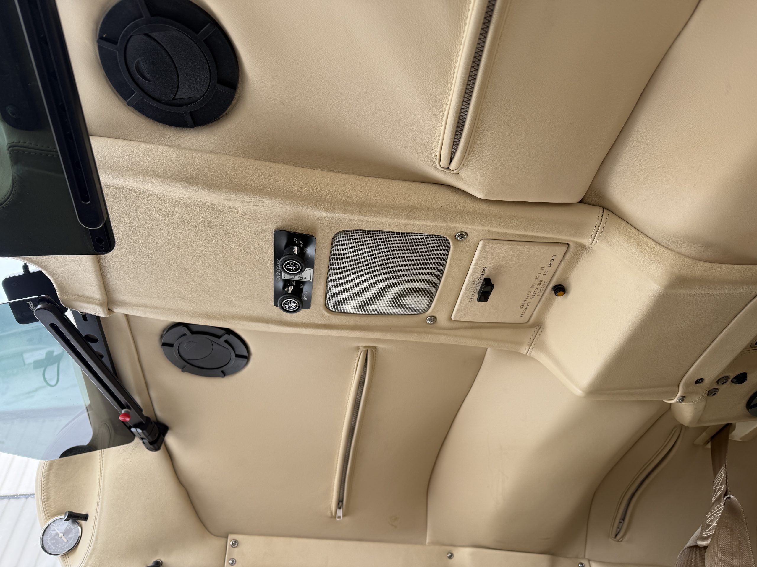 Beige car headliner with a circular overhead air vent zipper seam speaker grille and control switches on the ceiling panel