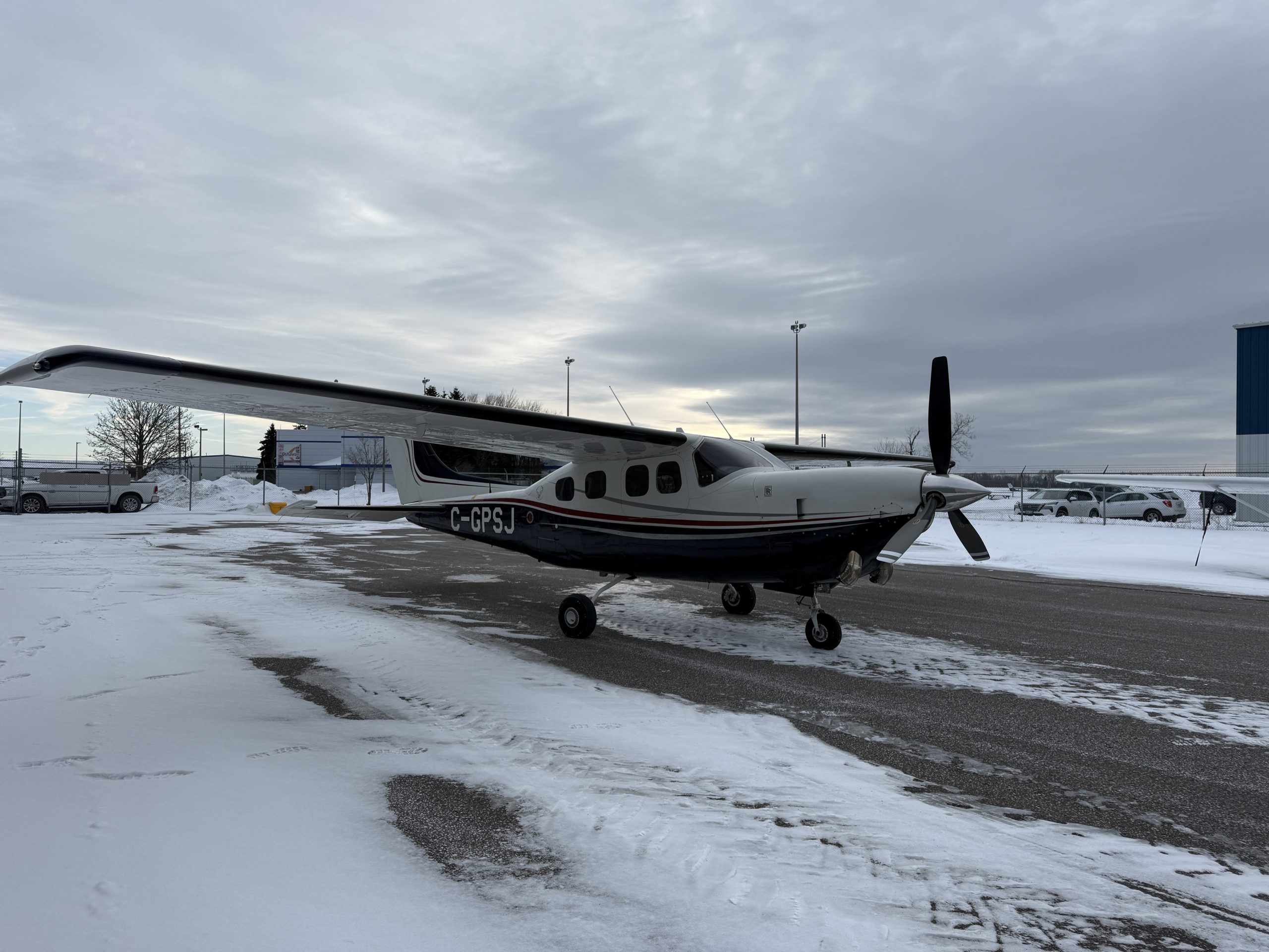 Small single engine propeller airplane parked on a snow covered airport tarmac under a cloudy sky