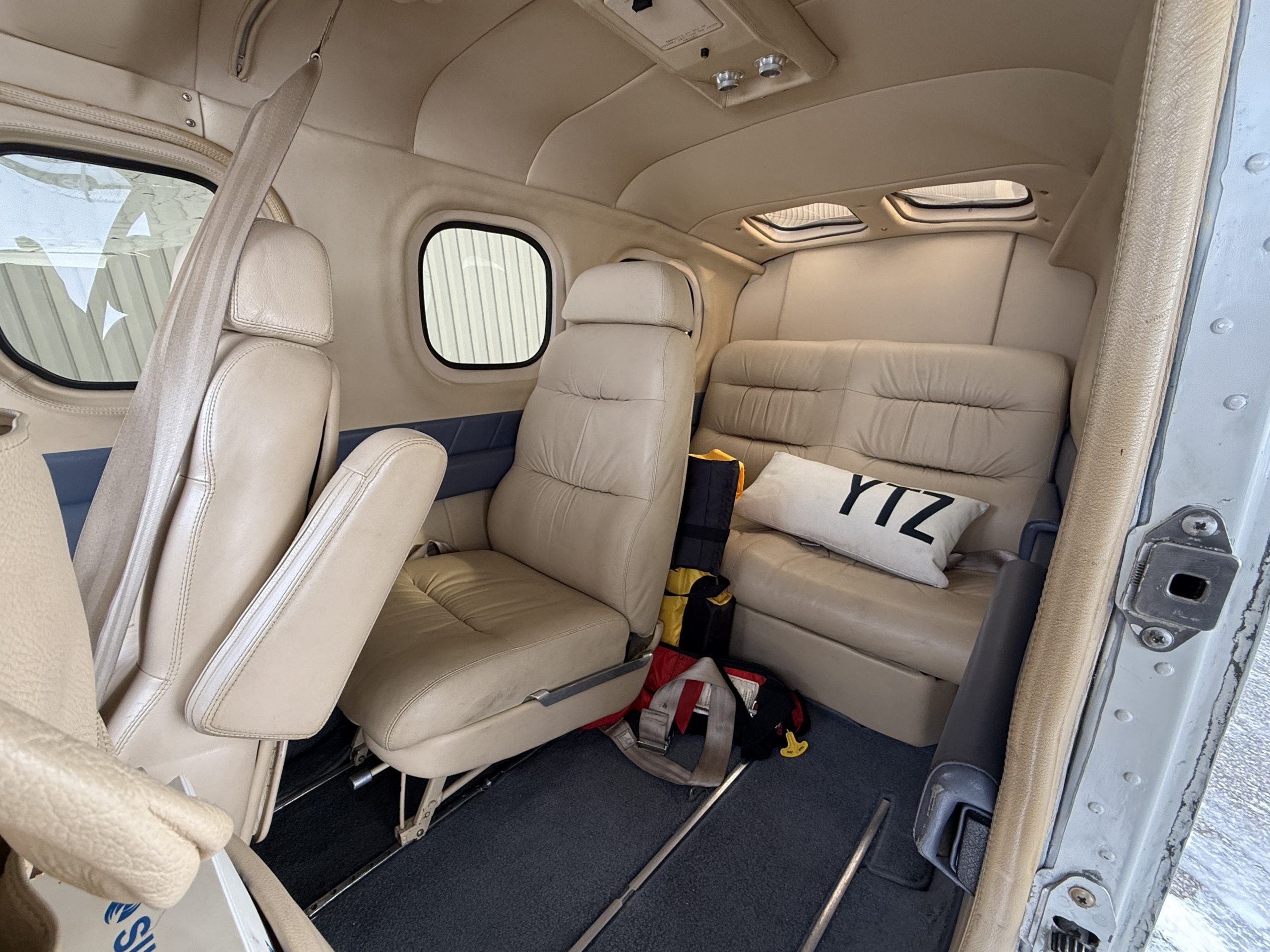 Beige leather airplane cabin interior with forward and rear seats window on left and life vests on the floor nearby