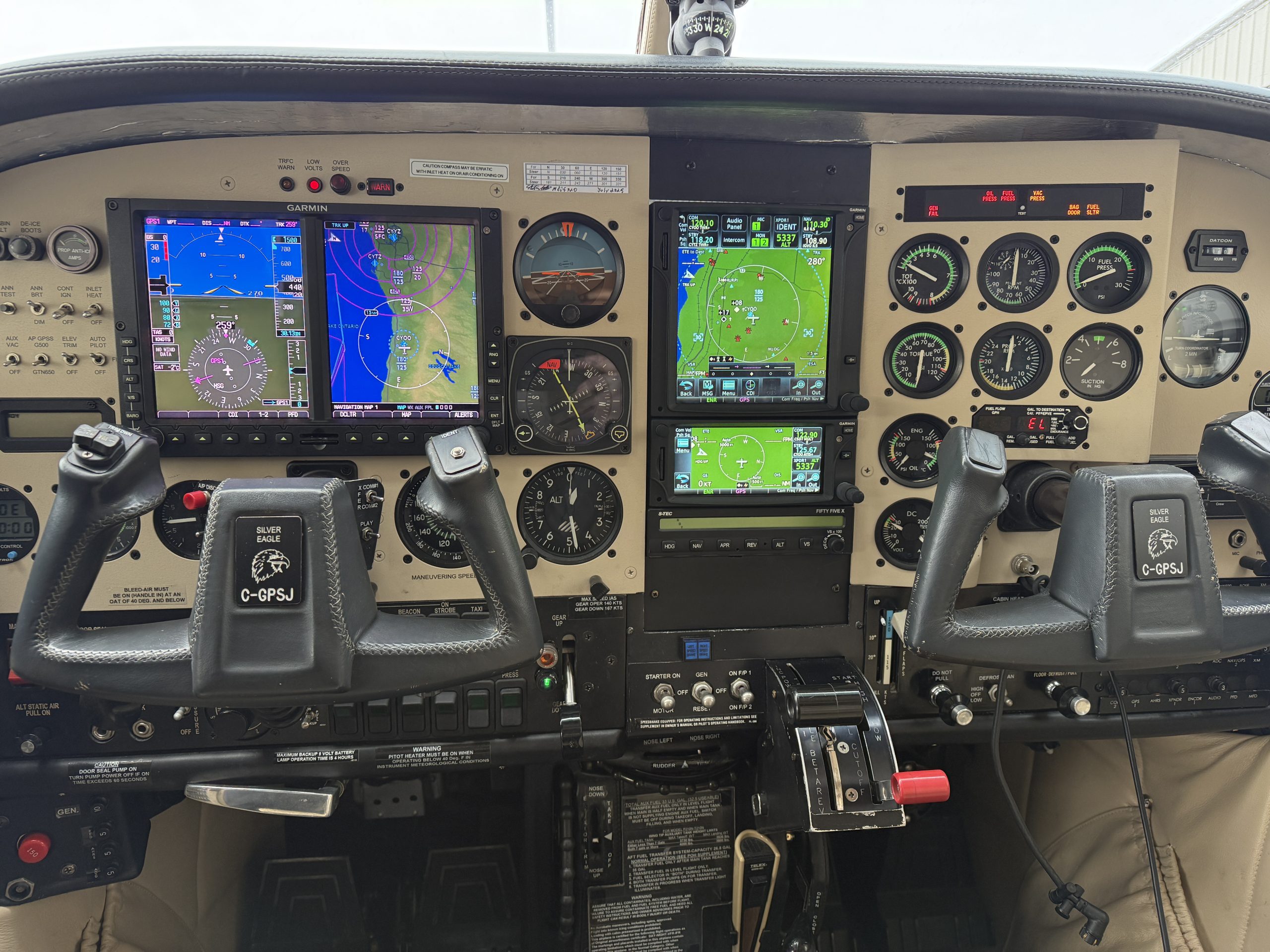 Modern aircraft cockpit dual Garmin glass flight displays with navigation maps and attitude indicators surrounded by assorted flight instruments and controls