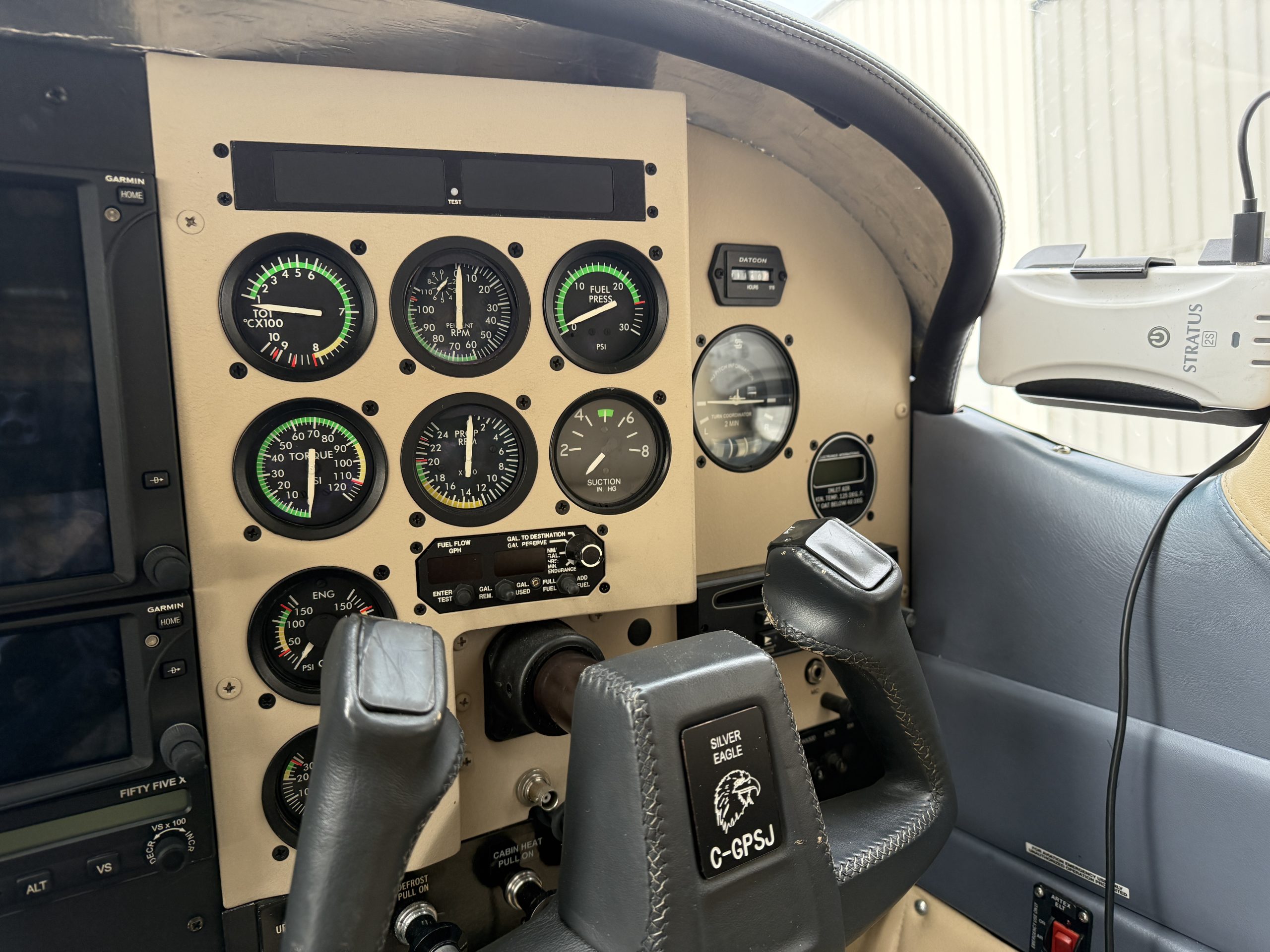 Cockpit instrument panel with round engine gauges green indicators dual control yokes and a Stratus GPS unit on the right