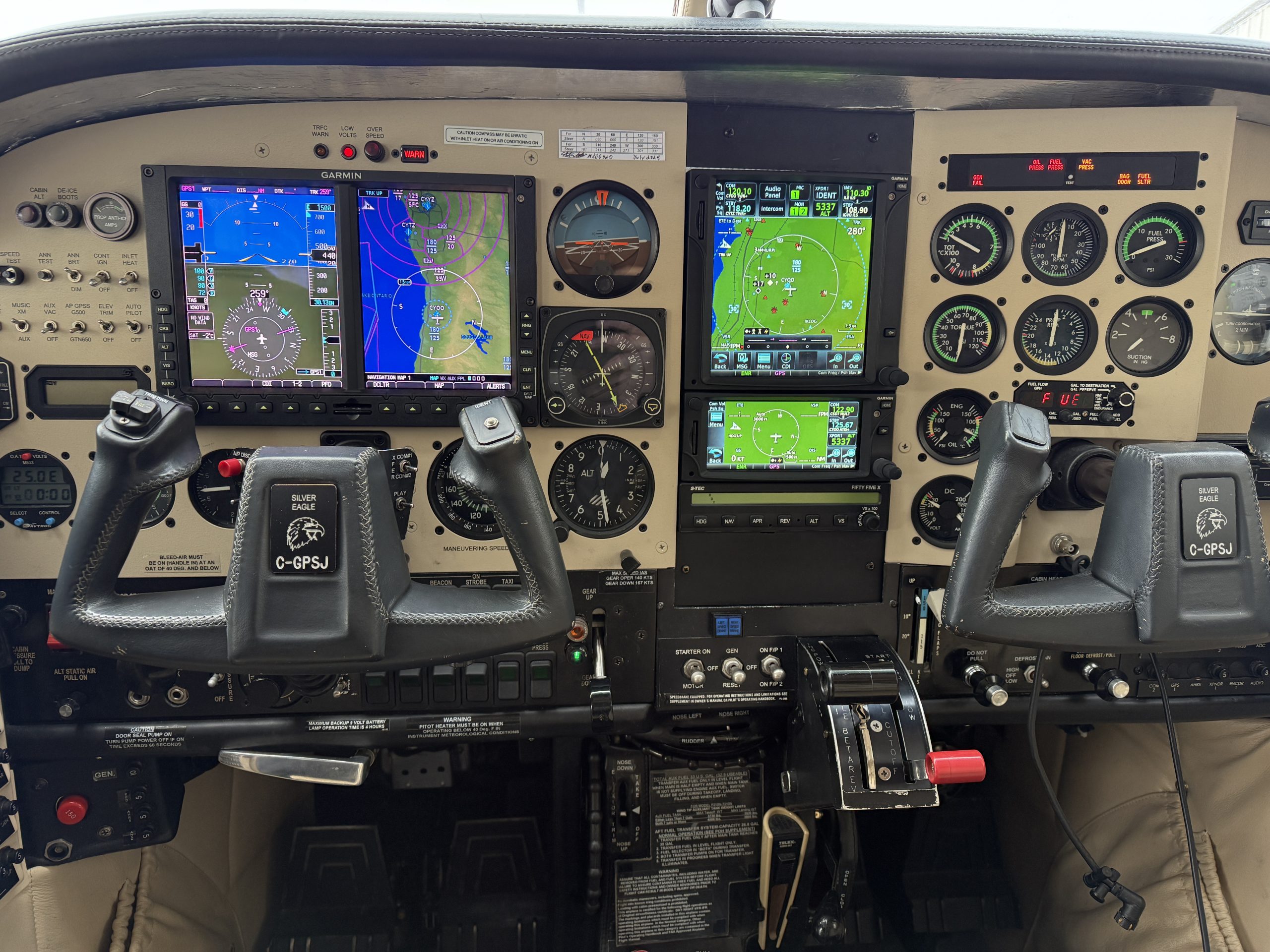Cockpit with dual Garmin glass cockpit displays showing navigation maps and attitude indicators plus many switches and gauges on the panel