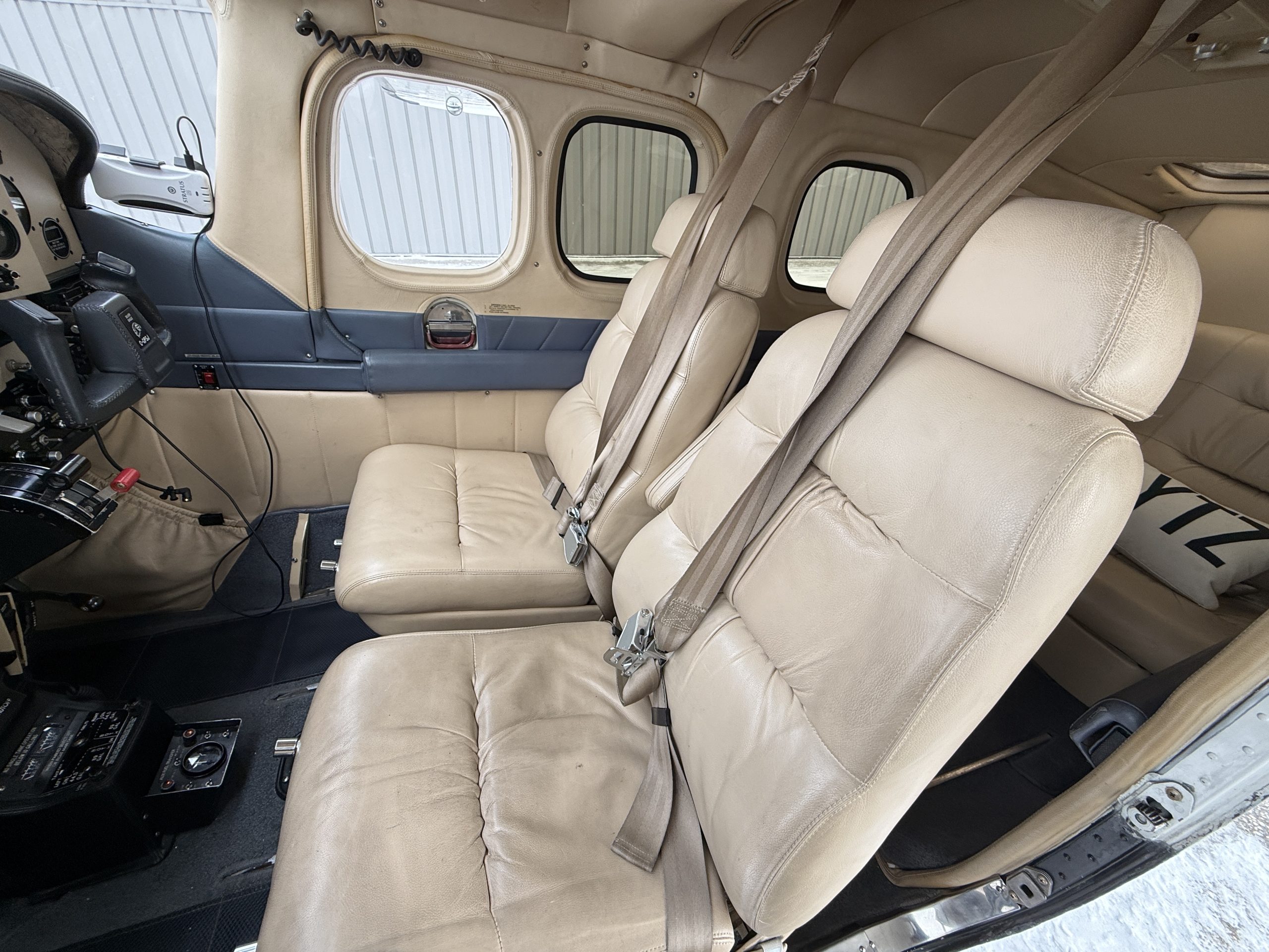 Interior of a small plane with beige leather seats cockpit controls and seat belts visible near the pilots area within the cabin
