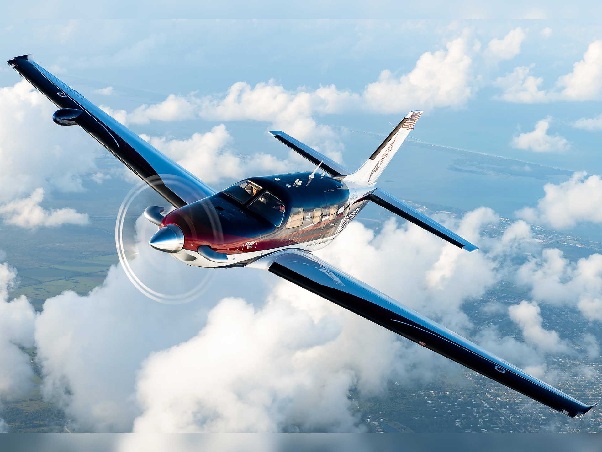 Blue and white single-engine propeller airplane in flight above fluffy clouds, cockpit windows visible.