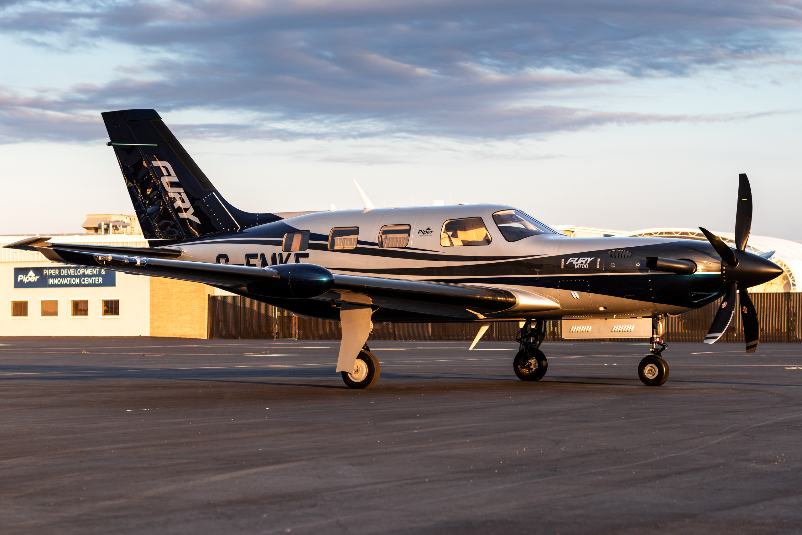 Piper Fury M700 private airplane parked on the tarmac with a hangar in the background at an airport.
