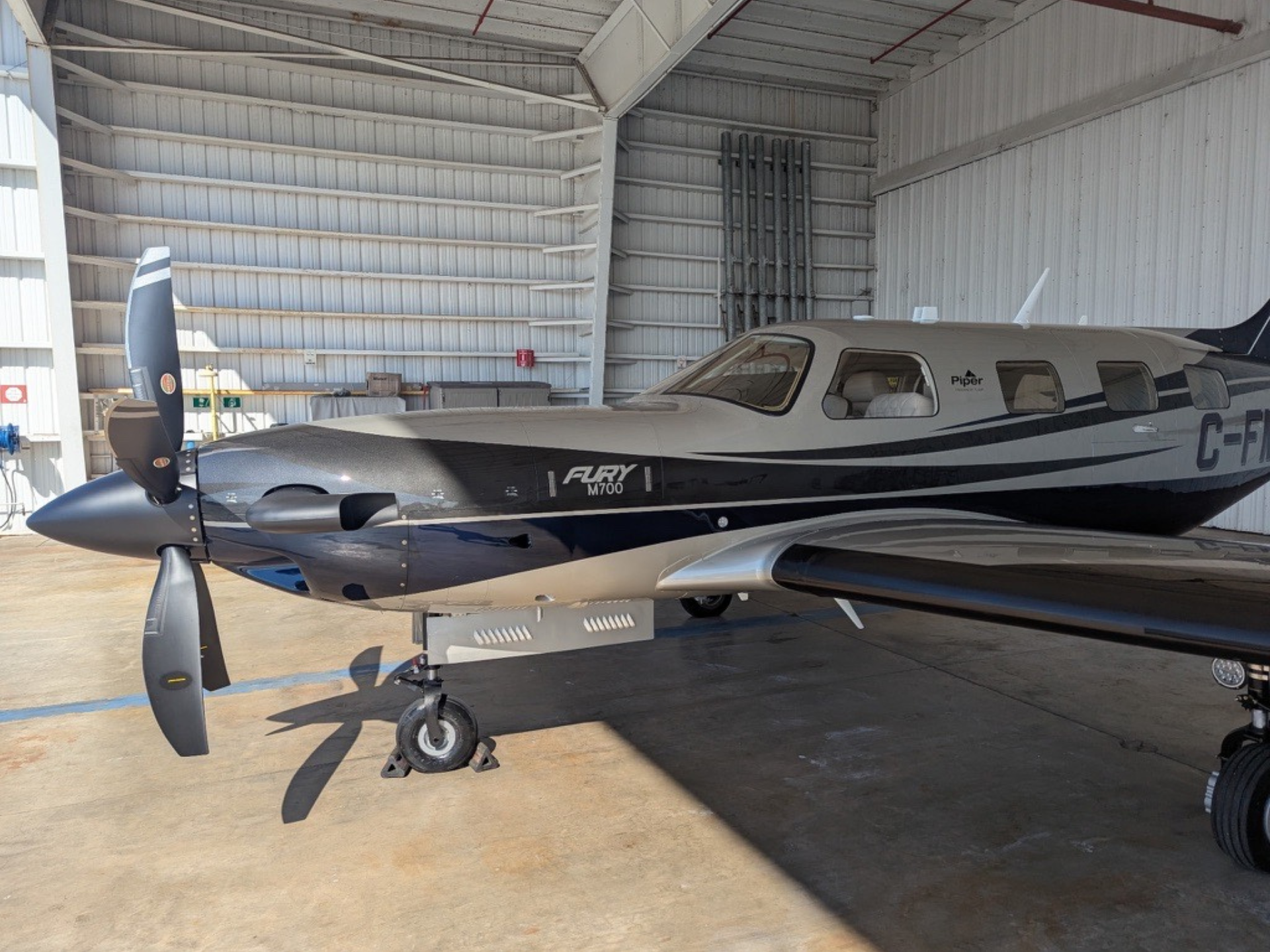 Side view of a small turboprop airplane in a hangar, propeller at the nose and landing gear visible in front.