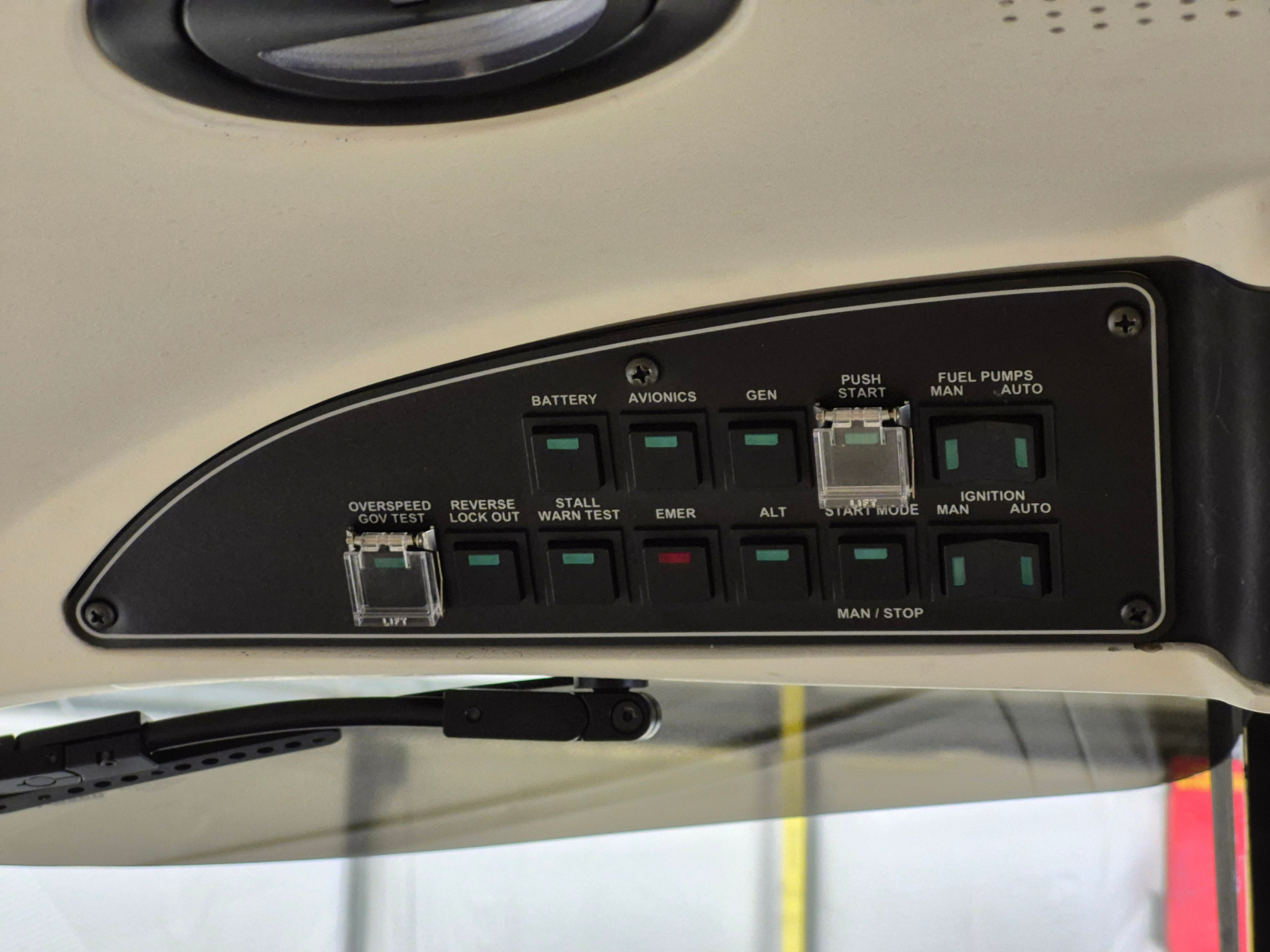 Overhead aircraft cockpit panel with labeled switches: Battery, Avionics, Gen, Push Start, and Fuel Pumps (Man/Auto) with green indicator toggles and a clear plastic latch switch at center-right.