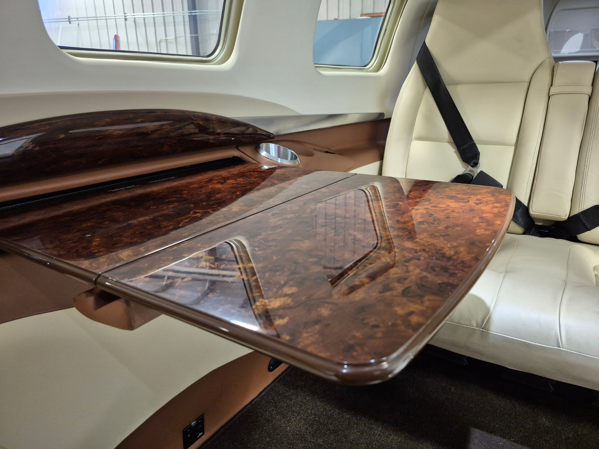 Luxurious private jet interior with a glossy wooden table, beige leather seats, and a seat belt.