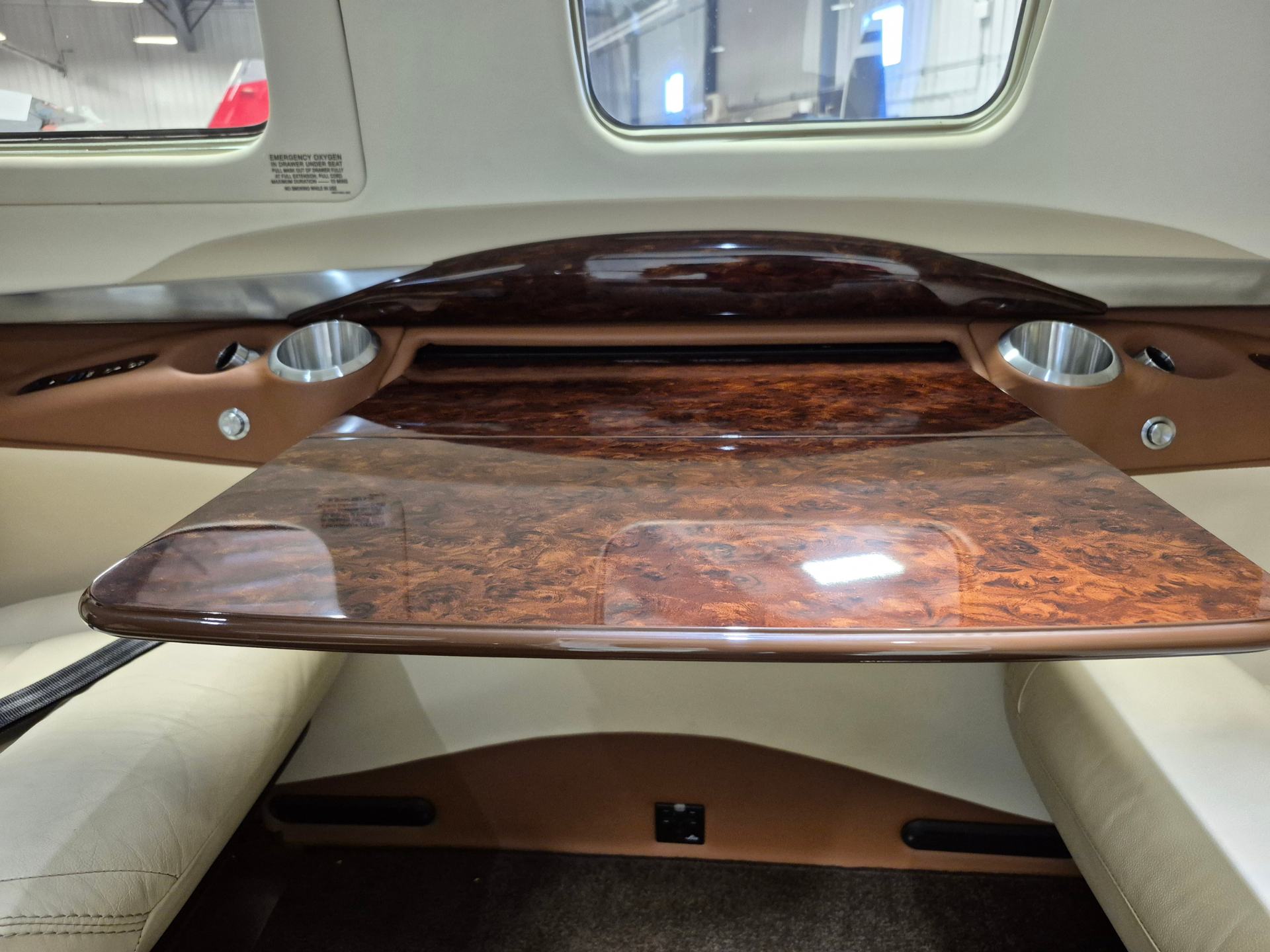 Luxurious car rear cabin with a glossy wood veneer table and beige leather seating, viewed through side windows.