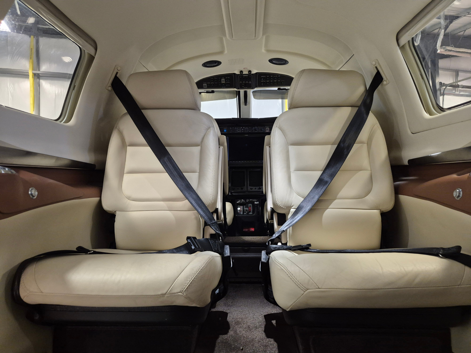 Interior of a small private airplane showing beige leather seats with seat belts and a cockpit at the front, windows on both sides visible.