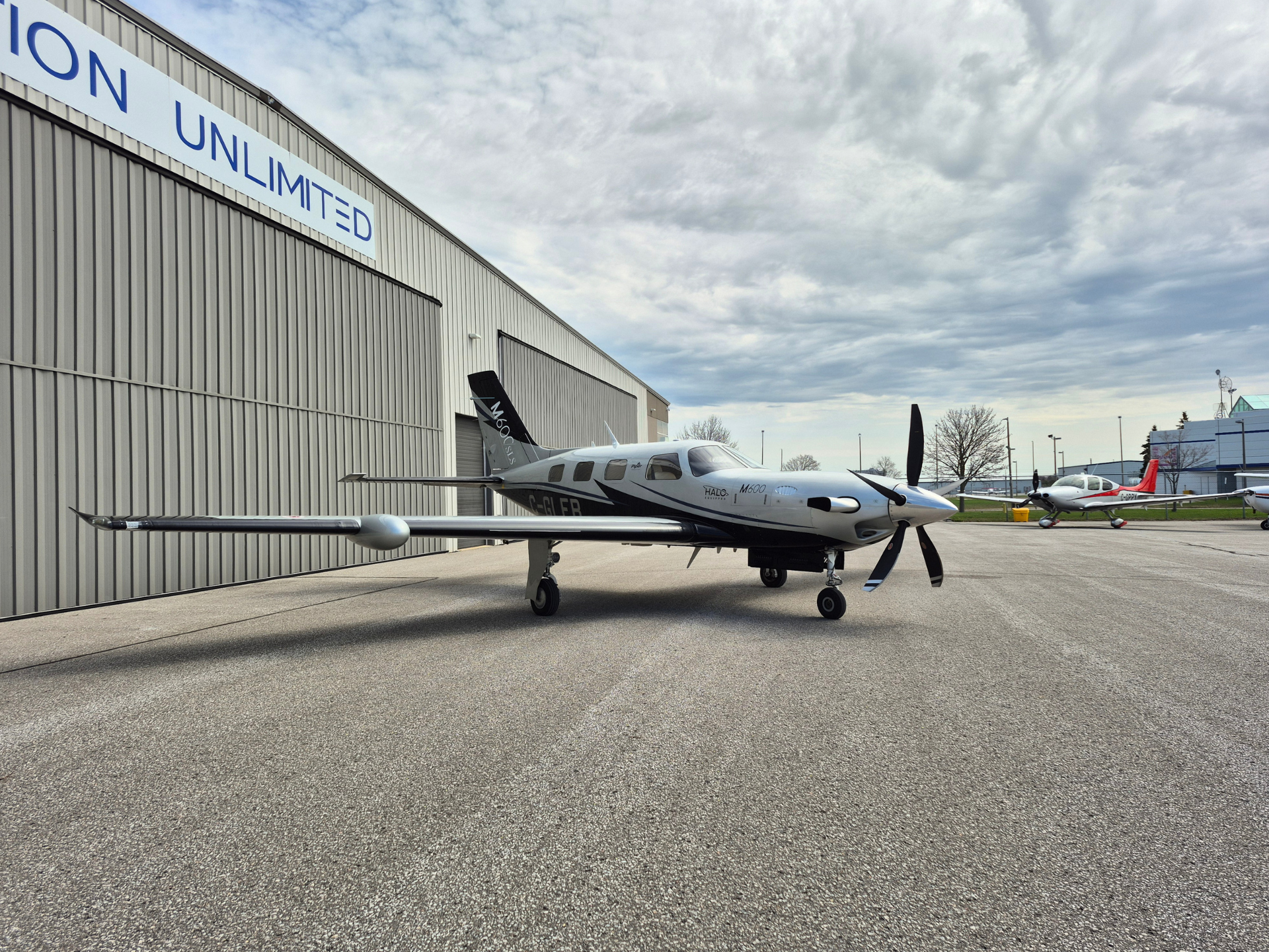 Twin-engine propeller airplane parked on a tarmac beside a corrugated metal hangar with a large UNLIMITED sign.