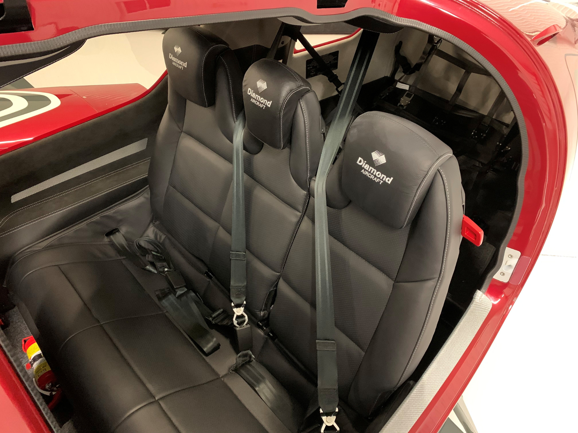 Interior of a red Diamond Aircraft cockpit showing two black passenger seats with harnesses and seat belts.
