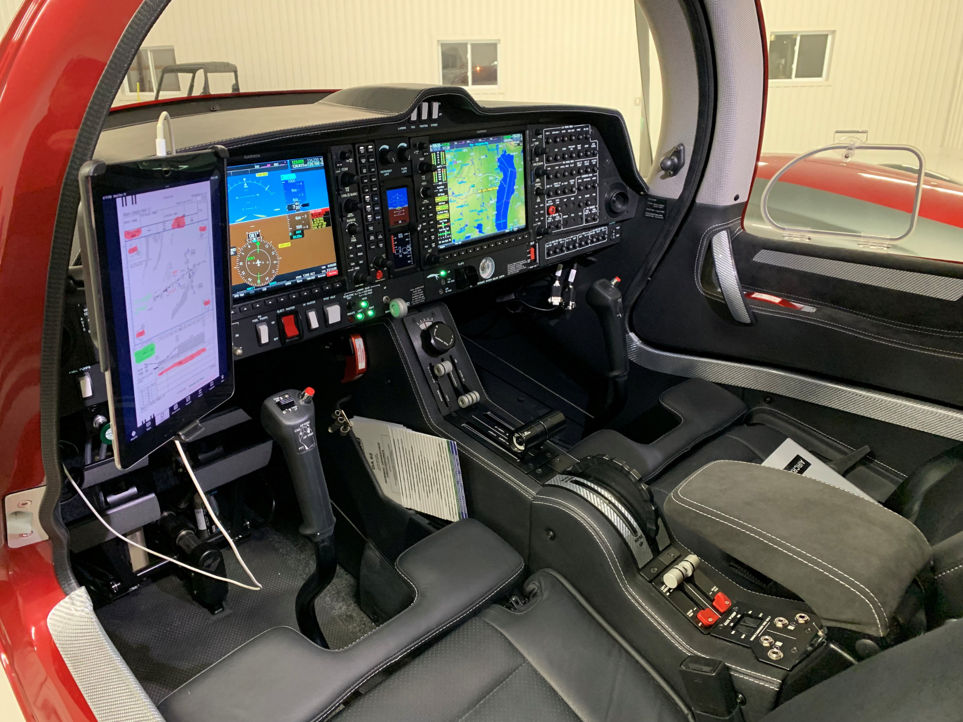 Modern aircraft cockpit with multiple Garmin screens and control panels inside a red-painted cabin.