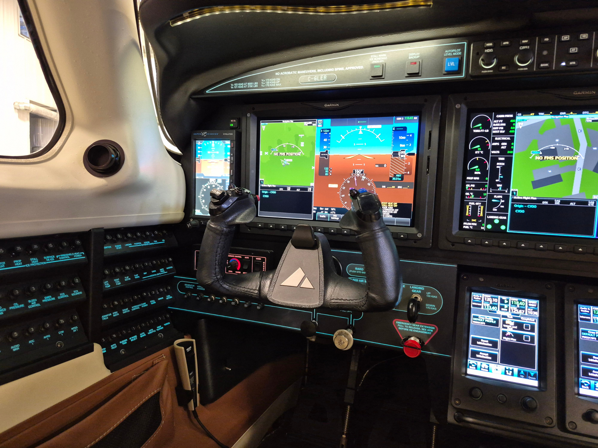 Inside aircraft cockpit with three large glass screens showing flight instruments and navigation, dual yokes, and Garmin branding on the panels.