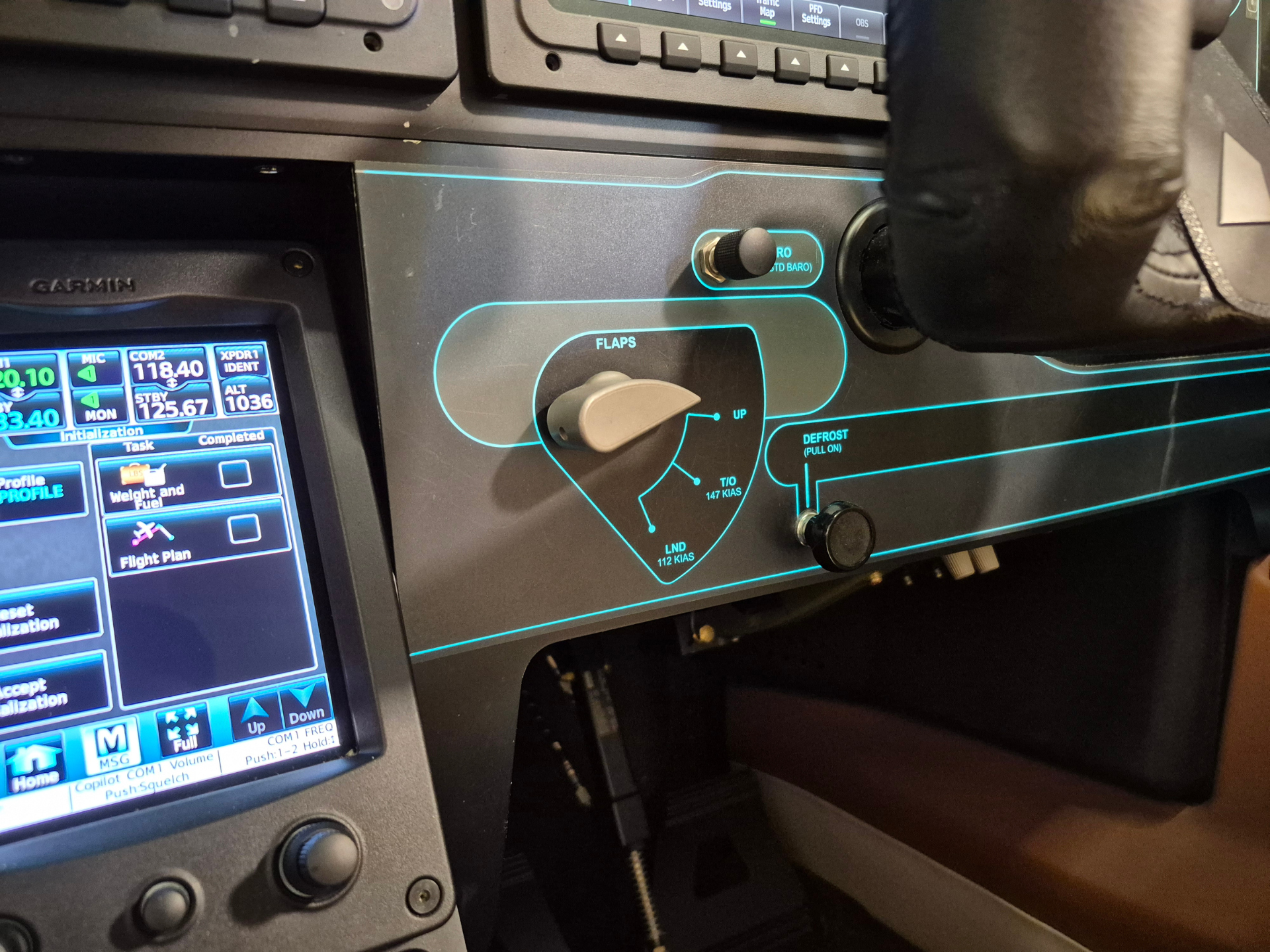 Cockpit panel with a touchscreen avionics display showing flight data beside a blue-outlined control panel labeled FLAPS and a rotary knob.