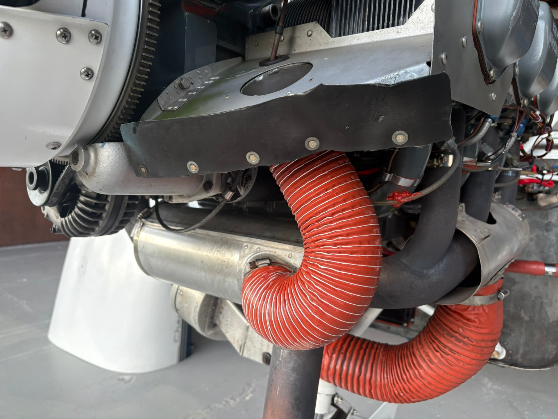 Close-up of aircraft engine area with a red corrugated duct, metal panels, and exposed bolts.