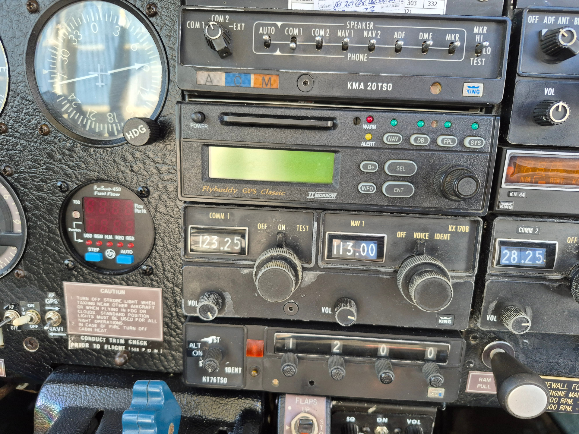 Close-up of a vintage aircraft cockpit panel with gauges, radios, and a Flybuddy GPS Classic unit in the center.